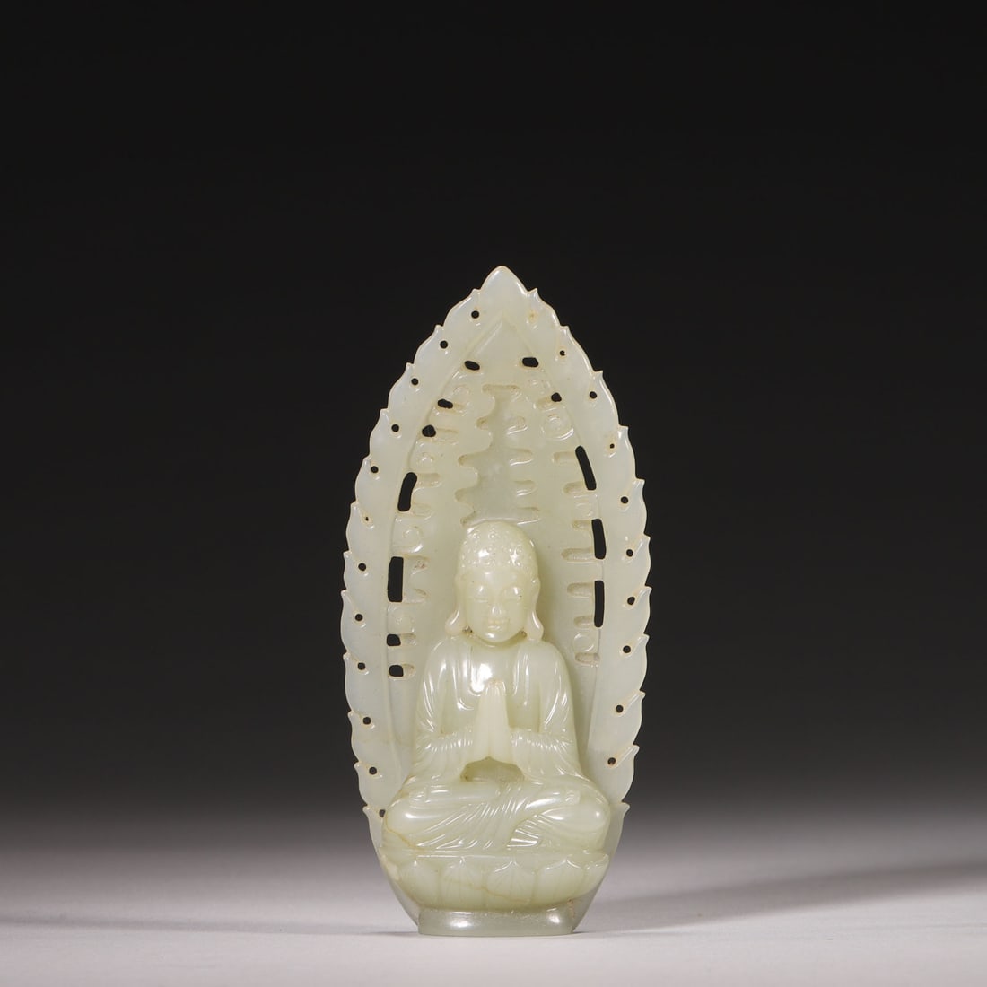 A Hetian Celadon Jade Seated Shakyamuni Buddha Statue, Qing Dynasty: H 11cm (4.33 in); Wt 58g (0.13 lb)A Hetian celadon jade seated Shakyamuni Buddha statue, carved with neat spiral hair, a serene face, wearing a kasaya, sitting cross-legged on a lotus throne with hand