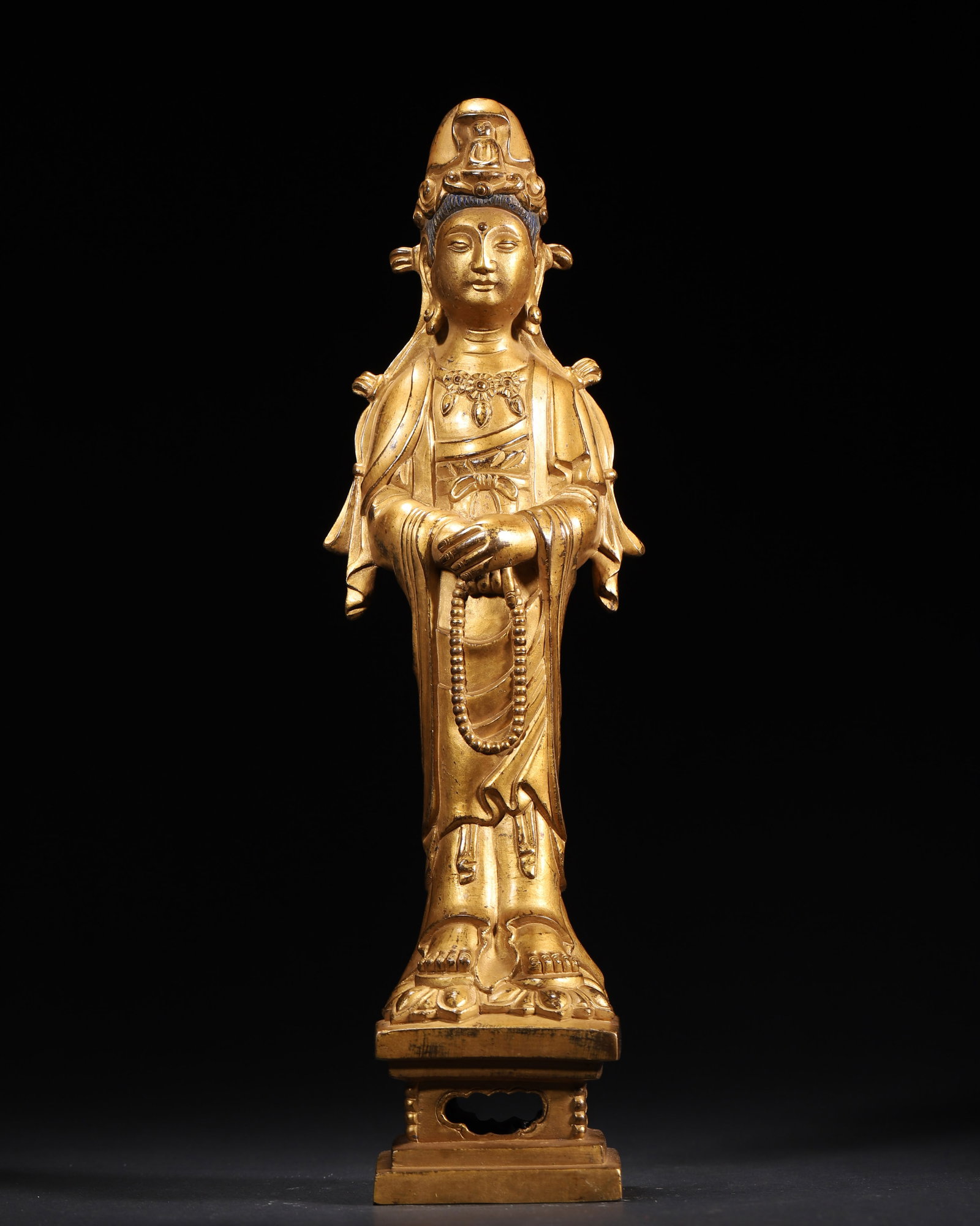 A Gilt-Bronze Standing Statue of Guanyin Bodhisattva, Qing Dynasty: 9.0 x 6.0 x 30.0 cm (3.54 x 2.36 x 11.81 in), WT 1695.0 g (3.74 lb)A gilt-bronze standing statue of Guanyin Bodhisattva, Qing Dynasty. The serene Guanyin holds prayer beads, with a small Buddha on her