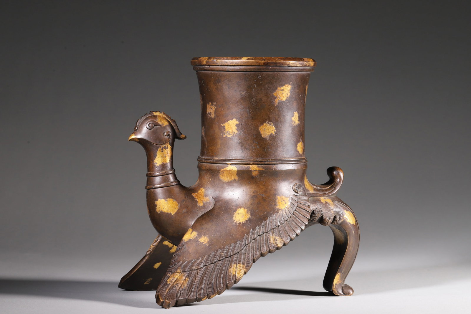 A Gilt Bronze Phoenix Vessel - Qing Dynasty: Length 17.0cm (6.69in), Width 13.0cm (5.12in), Height 19.0cm (7.48in), Weight 2737.0g (6.03lb)This phoenix vessel is cast in bronze with gilt spots, featuring a vivid phoenix posture. With exquisite c