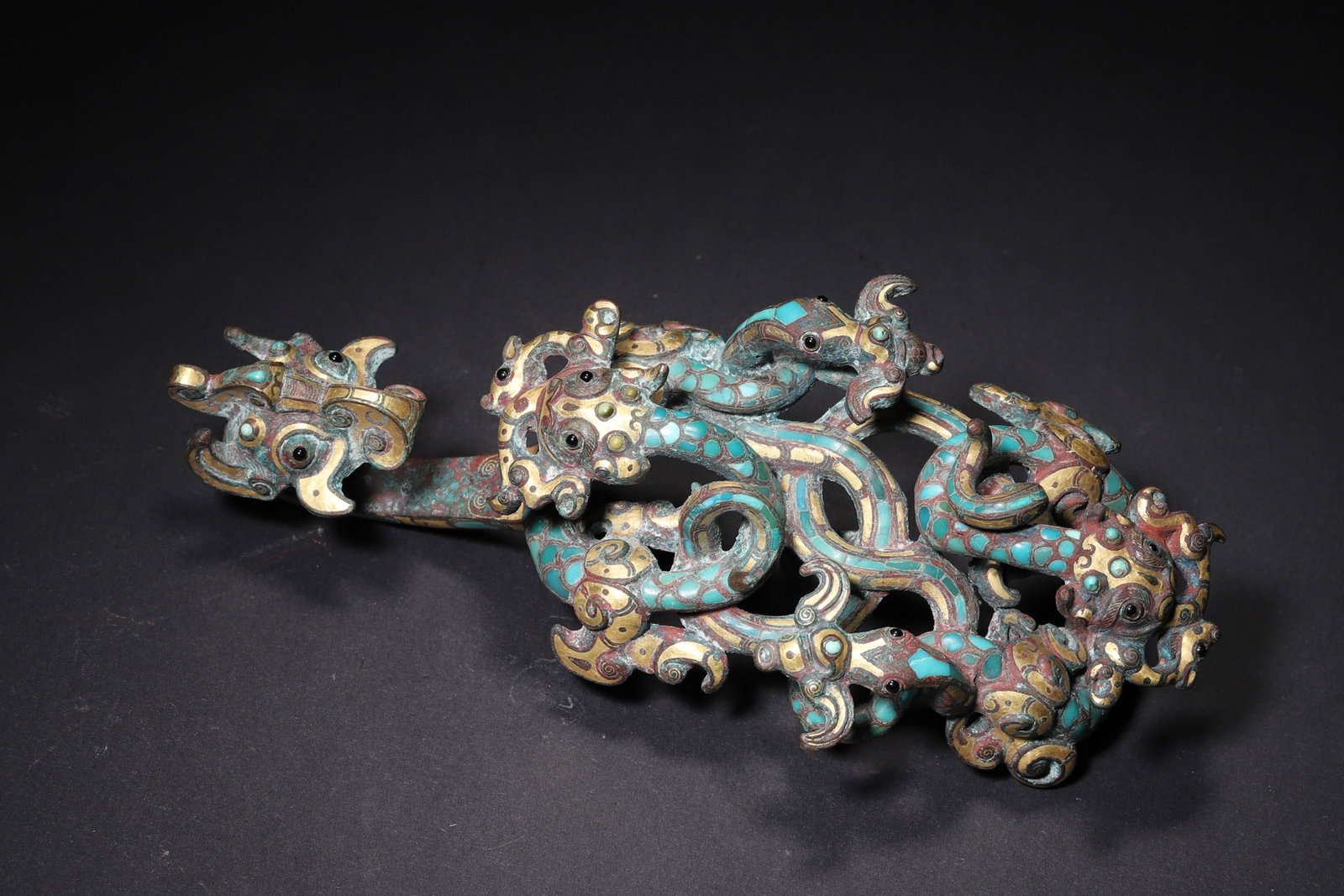 A Gold Inlaid Bronze Belt Hook with Turquoise and Openwork Dragon Pattern - Warring States Period: Length 18.0cm (7.09in), Width 8.0cm (3.15in), Weight 509.0g (1.12lb)A Warring States period openwork bronze belt hook with dragons, inlaid with gold and turquoise. The hook face features interwoven dr