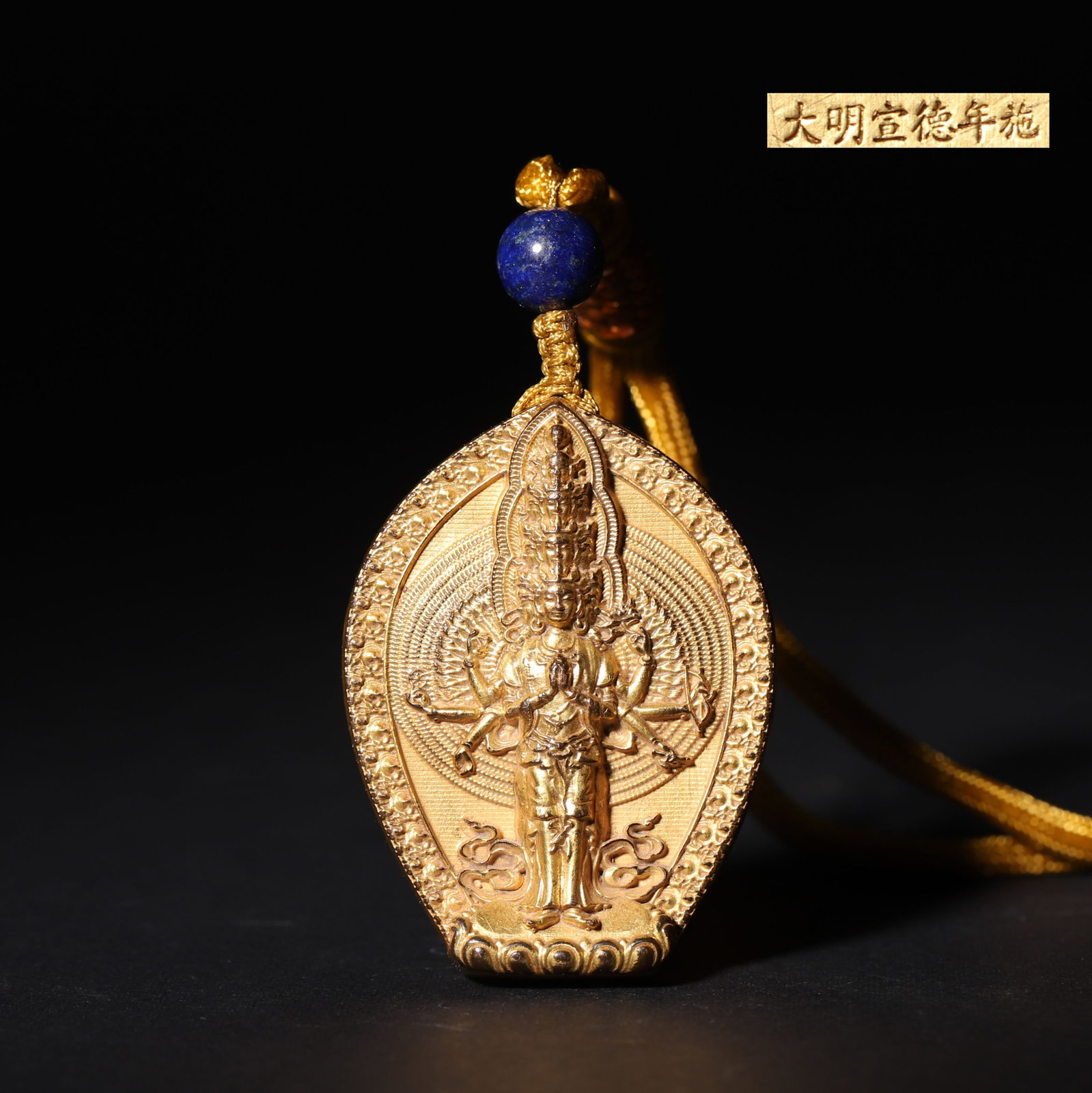 A Gilt Bronze Pendant of Thousand-Hand Guanyin, Xuande Period, Ming Dynasty: L 4.8cm (1.89 in); W 3.7cm (1.46 in); Wt 54g (0.12 lb)A gilt bronze pendant featuring a high-relief Thousand-Hand Guanyin on the obverse, with the deity in serene form, multiple arms outstretched, and