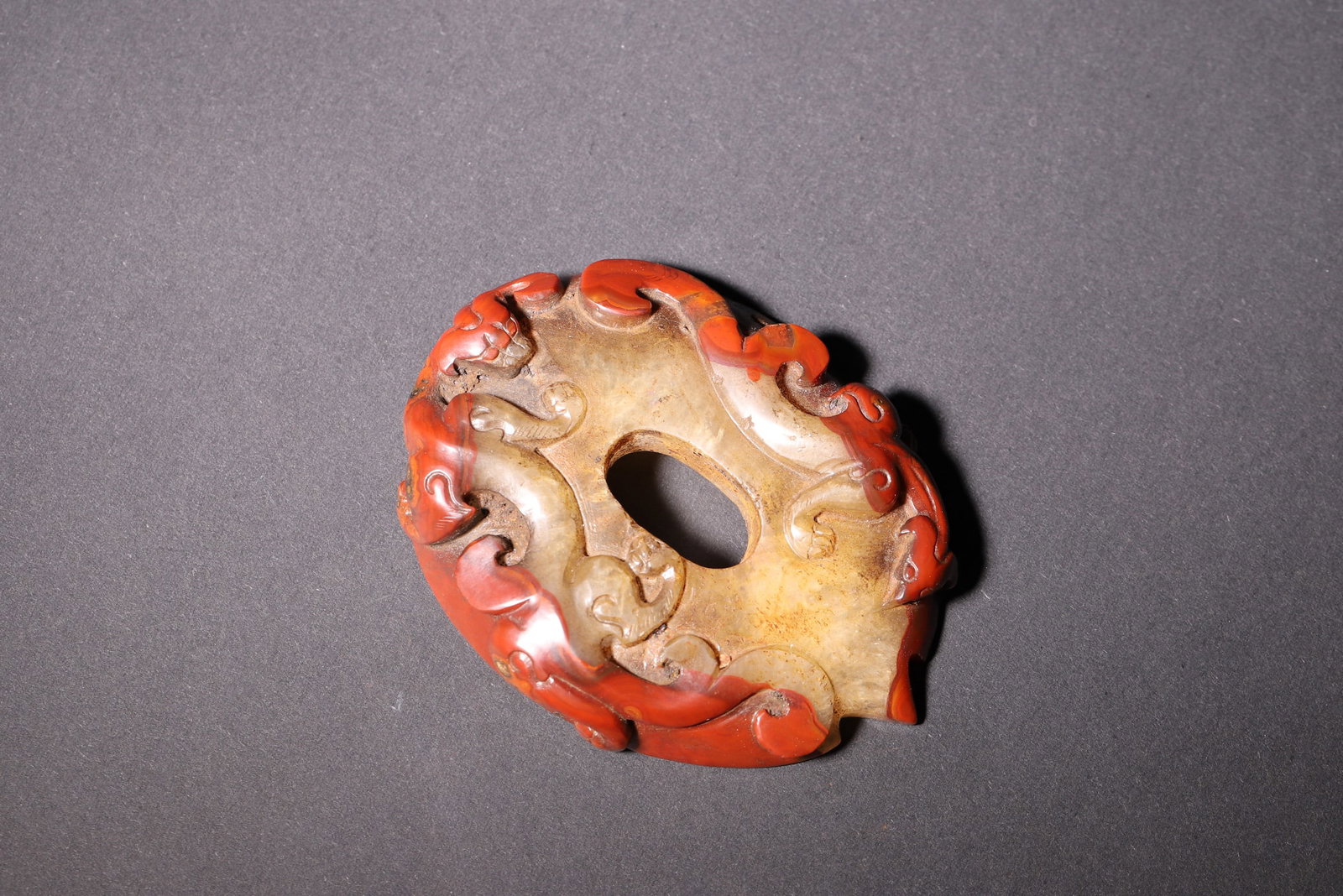 A red agate chilong-pattern she-shaped pendant, Han Dynasty: Length 8.0cm (3.15in), Width 6.2cm (2.44in), Weight 90.0g (0.2lb)This is a Han Dynasty red banded agate she-shaped pendant. Carved from rare red agate, it features an oval form with a central hole, ad