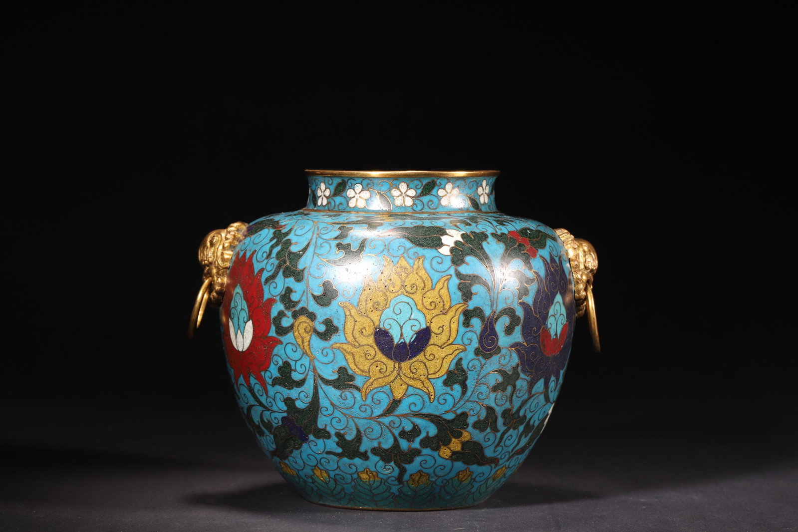 A Gilt-Bronze Cloisonné Enamel Jar with Interlocking Lotus and Animal Mask Handles, Ming Dynasty: Length 19.0cm (7.48in), Height 15.0cm (5.91in), Weight 1318.0g (2.91lb)A gilt-bronze cloisonné enamel jar from the Ming Dynasty, featuring animal mask handles with loose rings. The body is decorated 