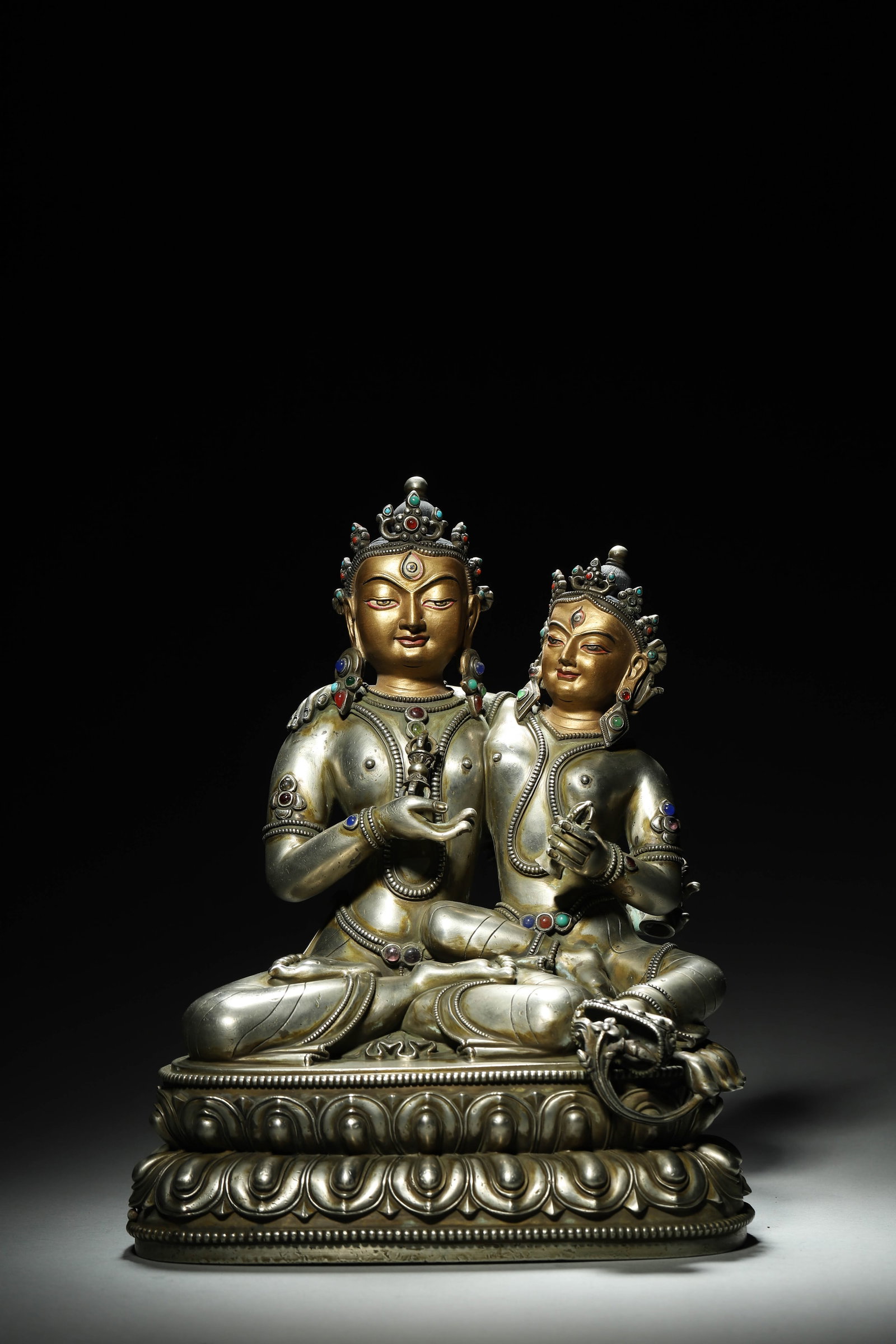 A Silver Gem-Inlaid Statue of Vajrasattva Consort, Qing Dynasty: L 24cm (9.45 in); H 32cm (12.6 in); Wt 7106g (15.67 lb)A Qing Dynasty silver gem-inlaid statue of Vajrasattva consort, with gilt faces and multi-colored gems. Seated in union, holding ritual implement