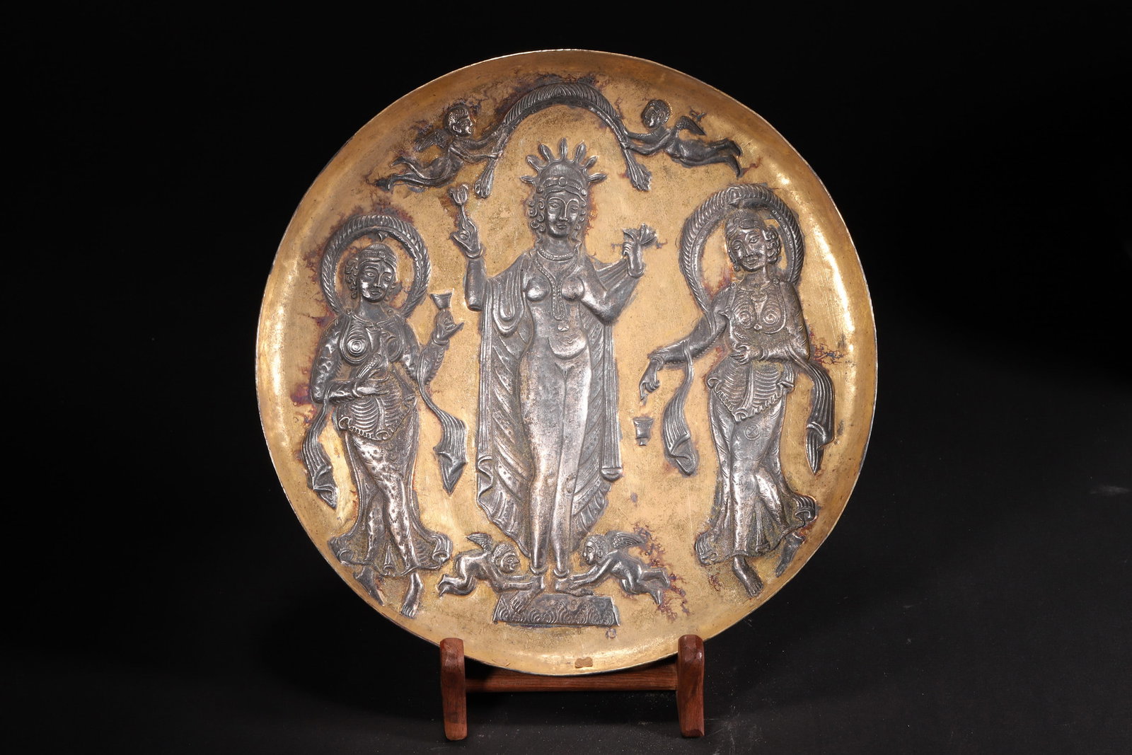 A Tang Dynasty Gilt Silver Plate with Western Goddess Motif: Diameter 21.0cm (8.27in), Weight 175.0g (0.39lb)A Tang Dynasty gilt silver plate, crafted with silver and partially gilded. The center features a relief of a Western goddess, flanked by attendants, wi