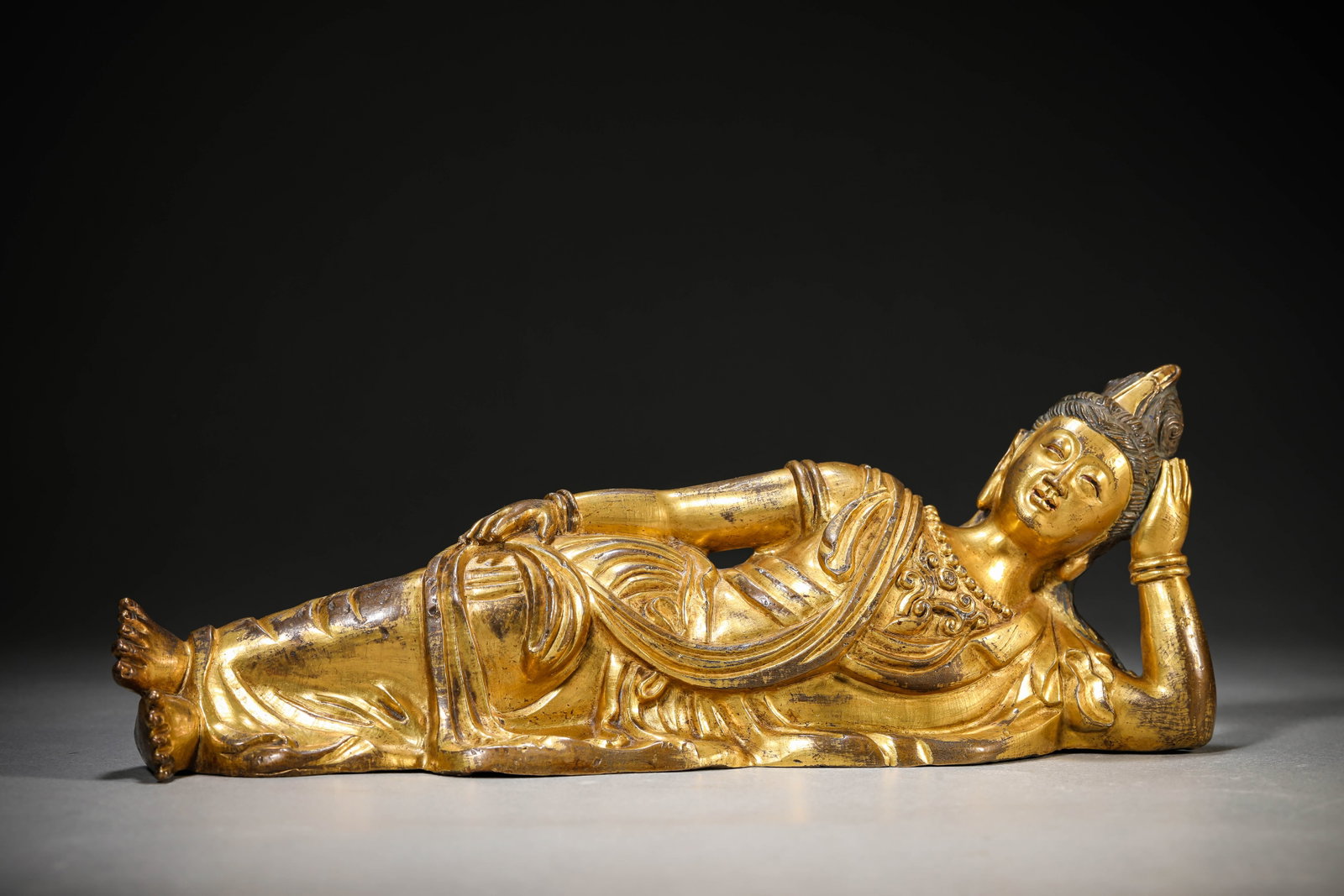 A Gilt-Bronze Reclining Figure of Buddha: Dimensions: Weight: 1036g. Length: 26.8 cm (10.55 in) x Width: 7.3 cm (2.87 in) x Height: 9.6 cm (3.78 in). All measurements are approximate.