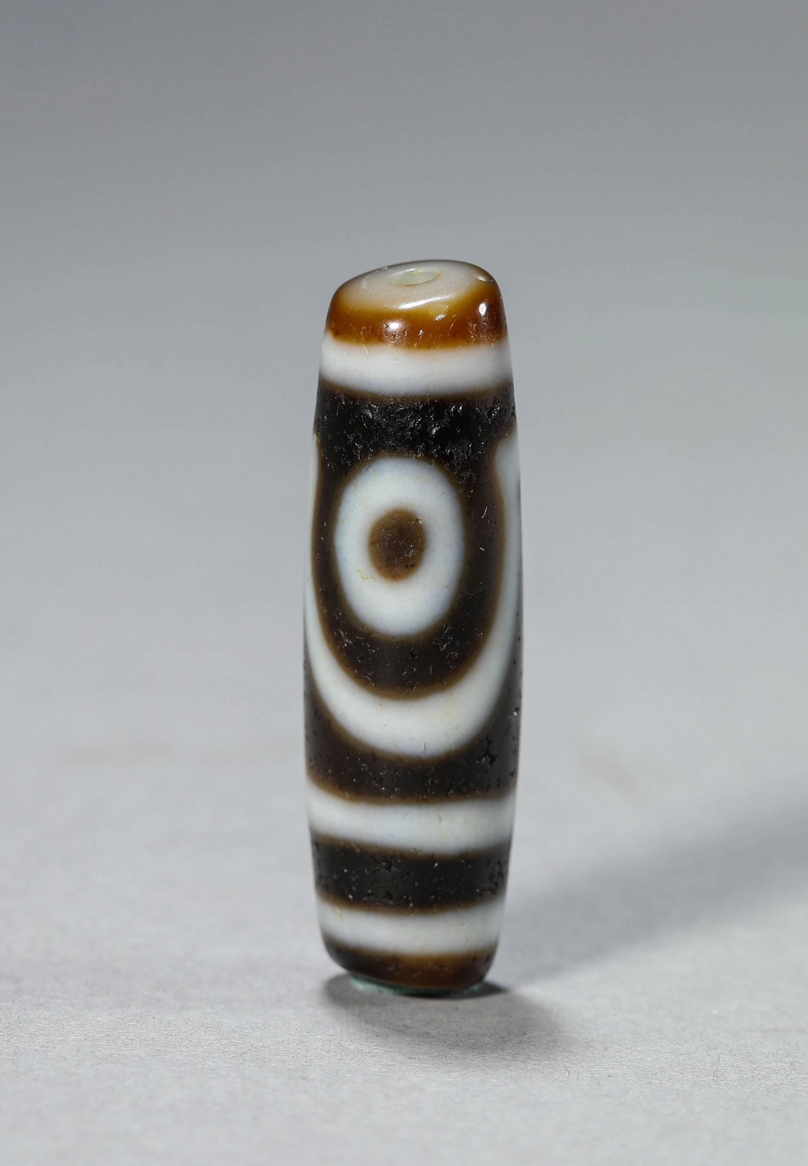 A Dzi Bead: Dimensions: Length: 3.8 cm (1.50 in) x Width: 1.1 cm (0.43 in). All measurements are approximate.