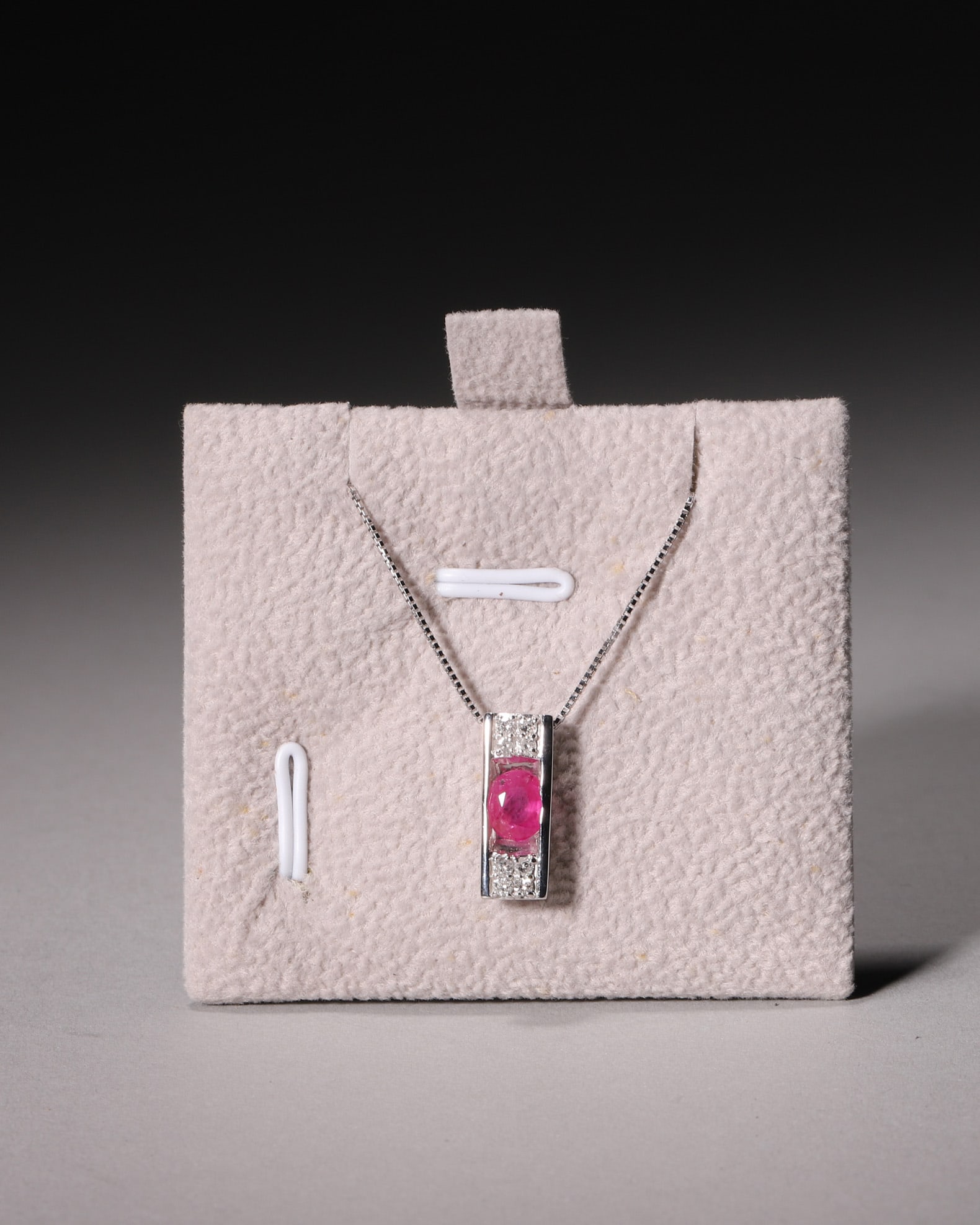 An 18K White Gold Rectangular Window Ruby Pendant Necklace with Diamond Halo: L 24.0cm (9.45 in); Wt 4.0g (0.01 lb)Crafted in polished 18K white gold with hollow rectangular frame, this pendant holds a vivid oval ruby capped with pave diamonds on top and bottom. Matched with fi