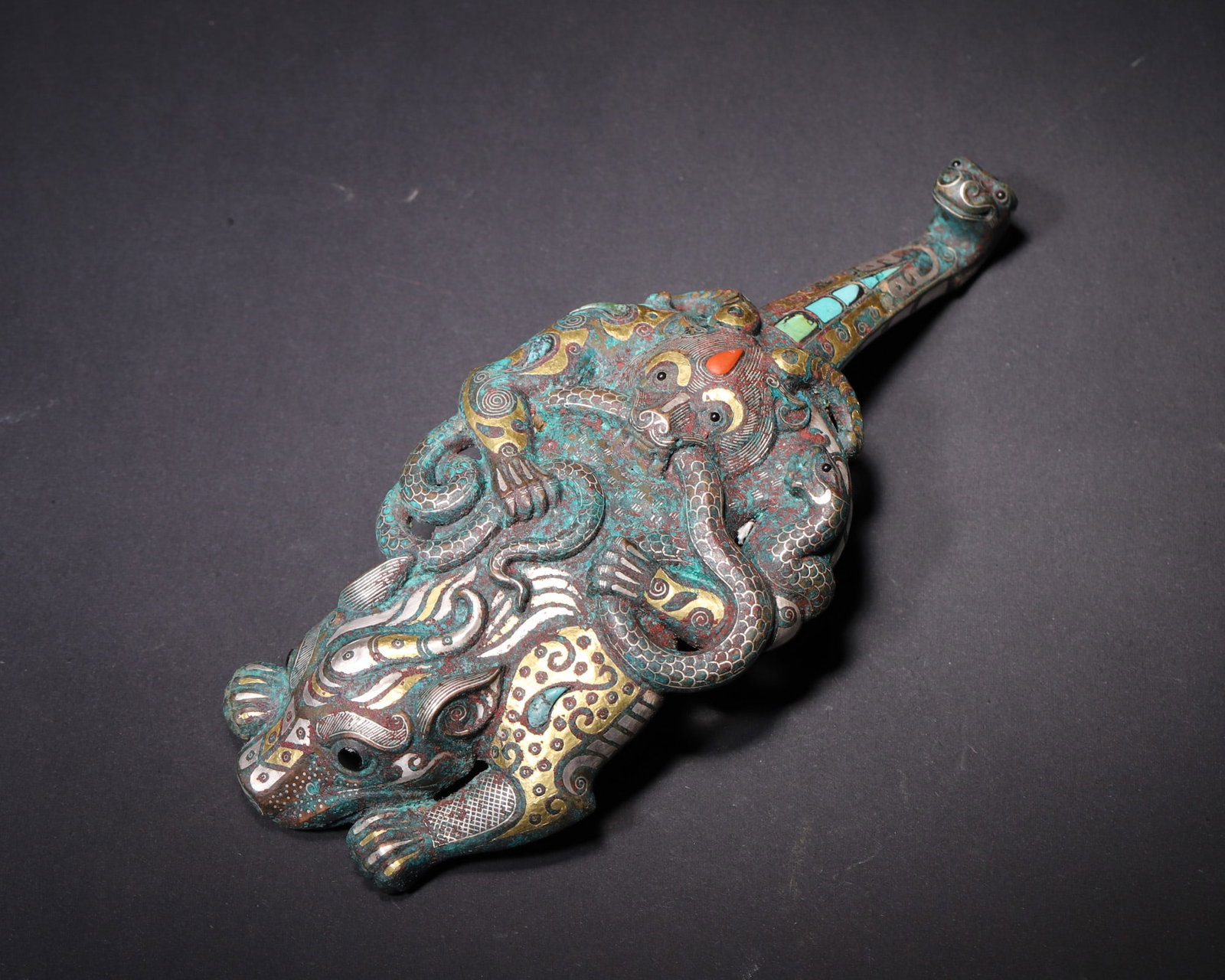A Gold and Silver Inlaid Bronze Belt Hook with Auspicious Beasts and Turquoise/Coral Inlays, Warring: L 8.2cm (3.23 in); Wt 798.0g (1.76 lb)A Warring States Period bronze belt hook exquisitely inlaid with gold, silver, turquoise and agate. Features tiger, monkey and snake motifs, natural patina and in