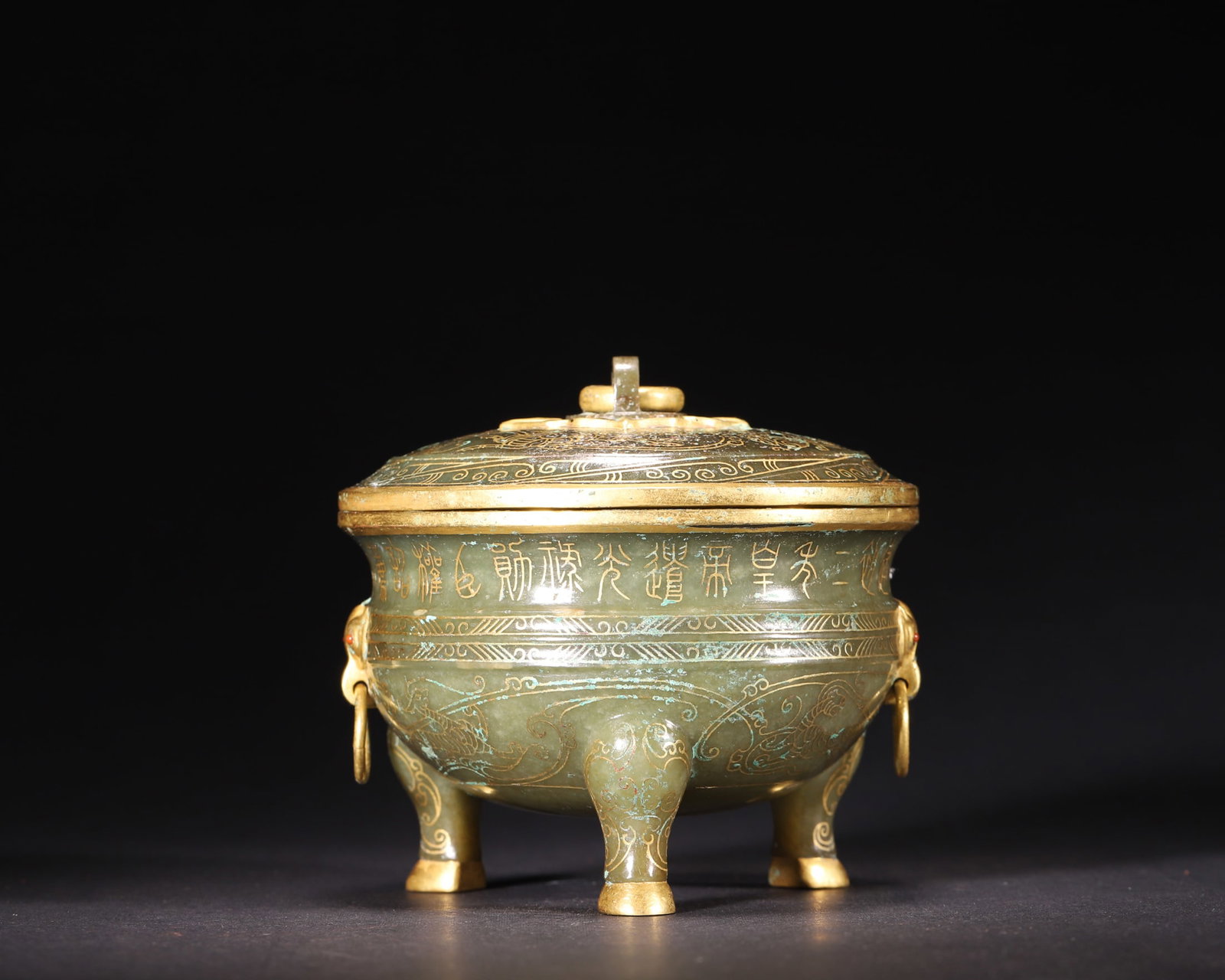A Hetian Celadon Jade Tripod Censer with Gold Inlaid Inscriptions and Beasts, Han Dynasty: D 10.5cm (4.13 in); H 9.0cm (3.54 in); Wt 440.0g (0.97 lb)A Han Dynasty Hetian celadon jade tripod censer with gold inlaid inscriptions and mythical beast patterns. It features gilt-bronze mounts and 