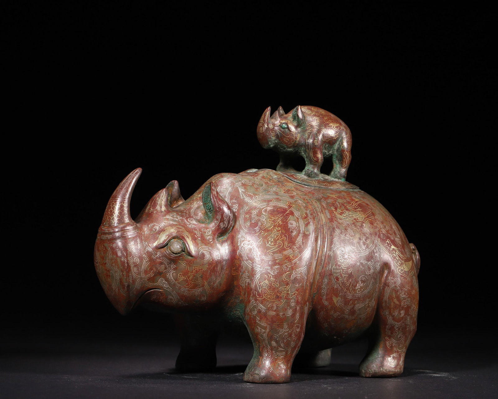 A Gold and Silver Inlaid Bronze Rhinoceros Vessel (Mother and Calf), Warring States Period: L 20.0cm (7.87 in); W 12.0cm (4.72 in); H 16.0cm (6.3 in); Wt 1869.0g (4.12 lb)A Warring States Period bronze vessel shaped as mother and calf rhinoceroses, inlaid with gold and silver. It features ex