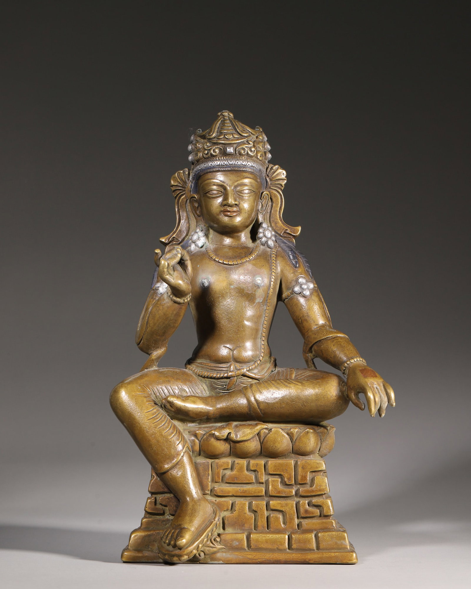 A Bronze Inlaid Silver Statue of Seated Avalokitesvara, Qing Dynasty: H 30cm (11.81 in); L 19cm (7.48 in); W 13.5cm (5.31 in); Wt 4130g (9.11 lb)This Qing Dynasty bronze seated Avalokitesvara features silver inlays on ornaments. With a serene face, the deity sits relaxe