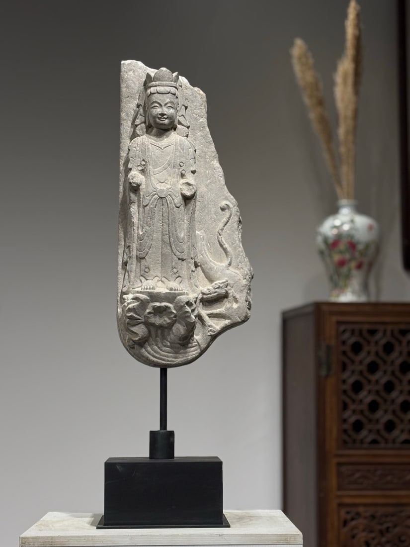 A LIMESTONE FRAGMENTARY STELE WITH RELIEF STANDING GUANYIN, NORTHERN QI DYNASTY: TotalHeight75cm NetBodyHeight50cm,Fragmentary limestone Buddhist stele of Northern Qi, carved with relief Guanyin standing on lotus base, a winding dragon carved on the side. Soft smooth carving lines