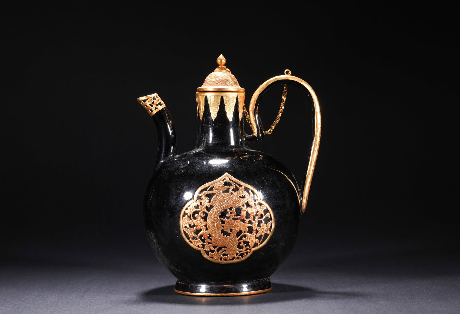 QING DYNASTY BLACK GOLD GLAZE OPENWORK AND HOLLOWED-OUT GILDED DRAGON PATTERN EWER: H:24.0cm(9.45in) W:18.0cm(7.09in)This ewer is a fine wine vessel of the Qing Dynasty imperial court. It features a flared mouth, straight neck, bulging belly, and foot ring, with a curved spout and ha