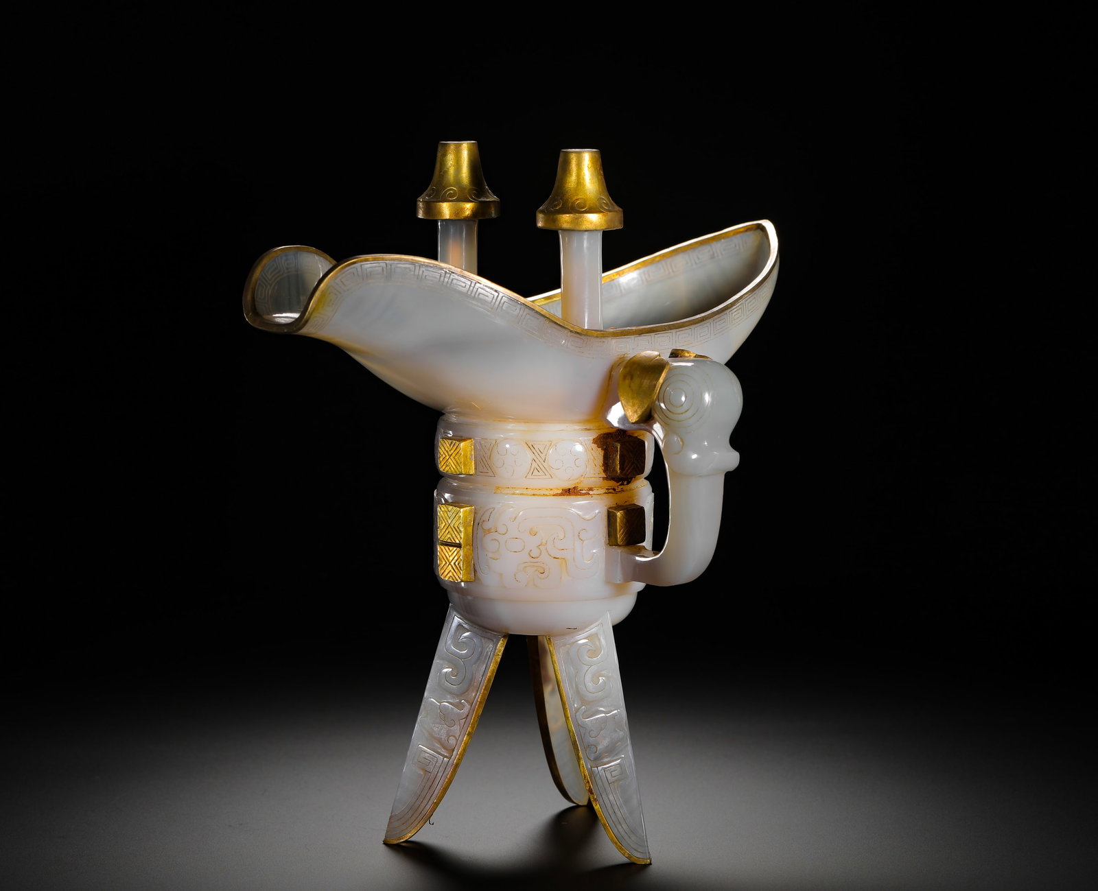 QING DYNASTY JADE GOBLET WITH GOLD INLAID AGATE AND ANIMAL FACE PATTERN: Height:22cm(8.66in) Width:21cm(8.27in) Weight:690g(1.52lb)Qing Dynasty white agate ritual jue wine vessel inlaid with gilt fittings, imitating Shang-Zhou bronze jue. Solid agate carving with two pilla