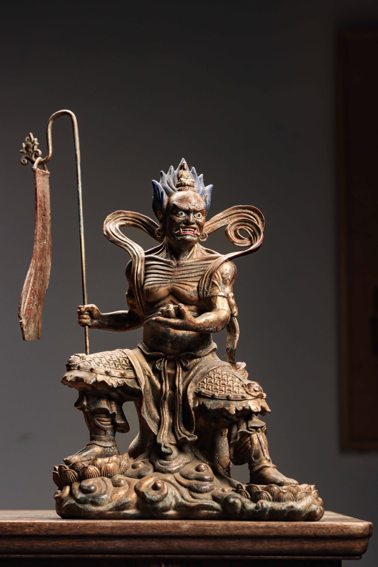 YUAN DYNASTY BRONZE LACQUER GOLD WRATHFUL GUARDIAN VAJRA SITTING FIGURE: Height:40cm(15.75in) Width:24cm(9.45in) Weight:4500g(9.92lb)Antique Yuan-Ming lacquered bronze wrathful guardian deity, staff with streamer, carved lotus cloud base, worn gilded surface, Buddhist stat