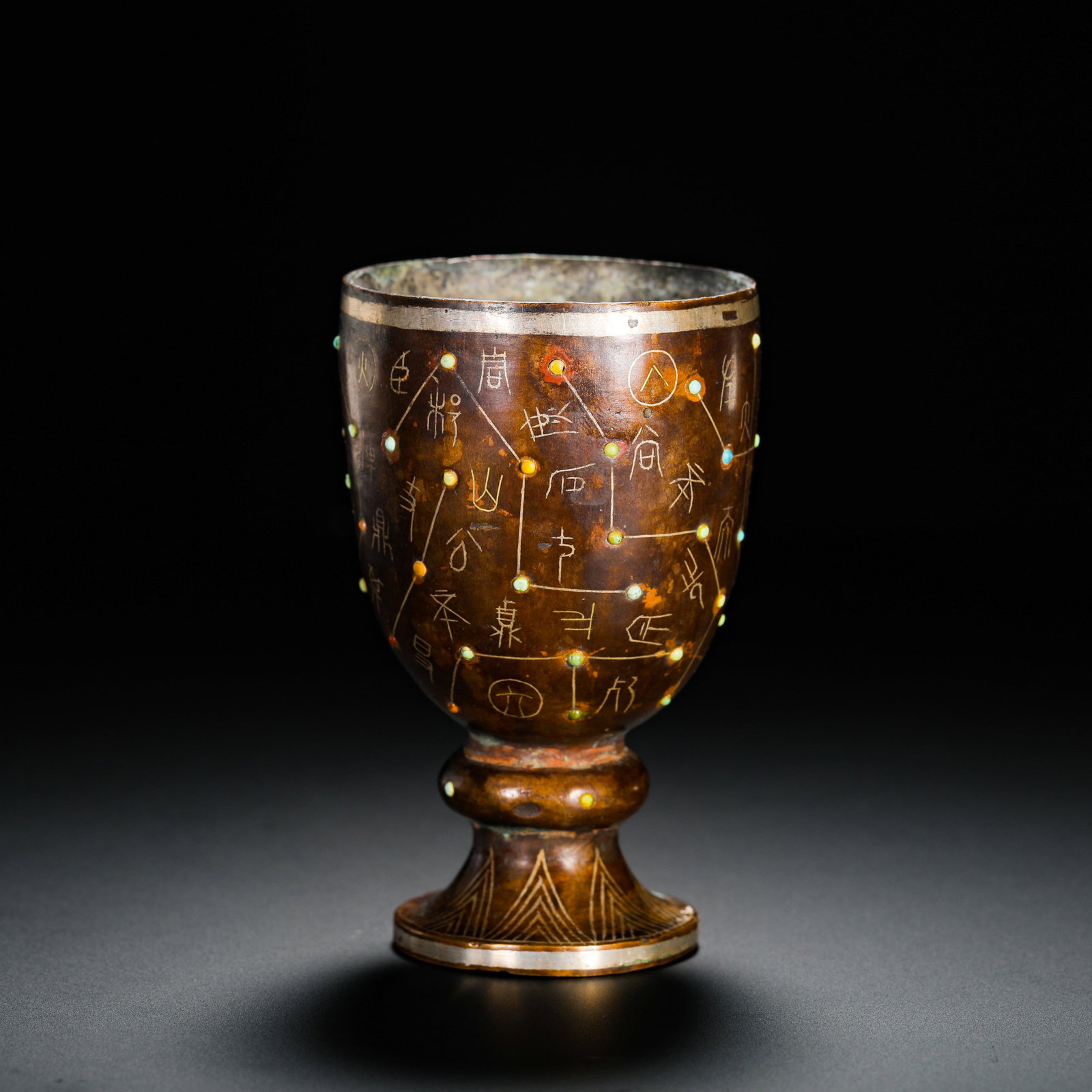A HIGH-FOOTED CUP WITH COPPER INLAID WITH GOLD AND TURQUOISE IN THE HAN DYNASTY: Height:9.5cm(3.74in) Width:6cm(2.36in) Weight:330g(0.73lb)Bronze high-foot cup inlaid with gold wire and turquoise celestial constellation patterns. Dark aged bronze patina covered the body, ancient s