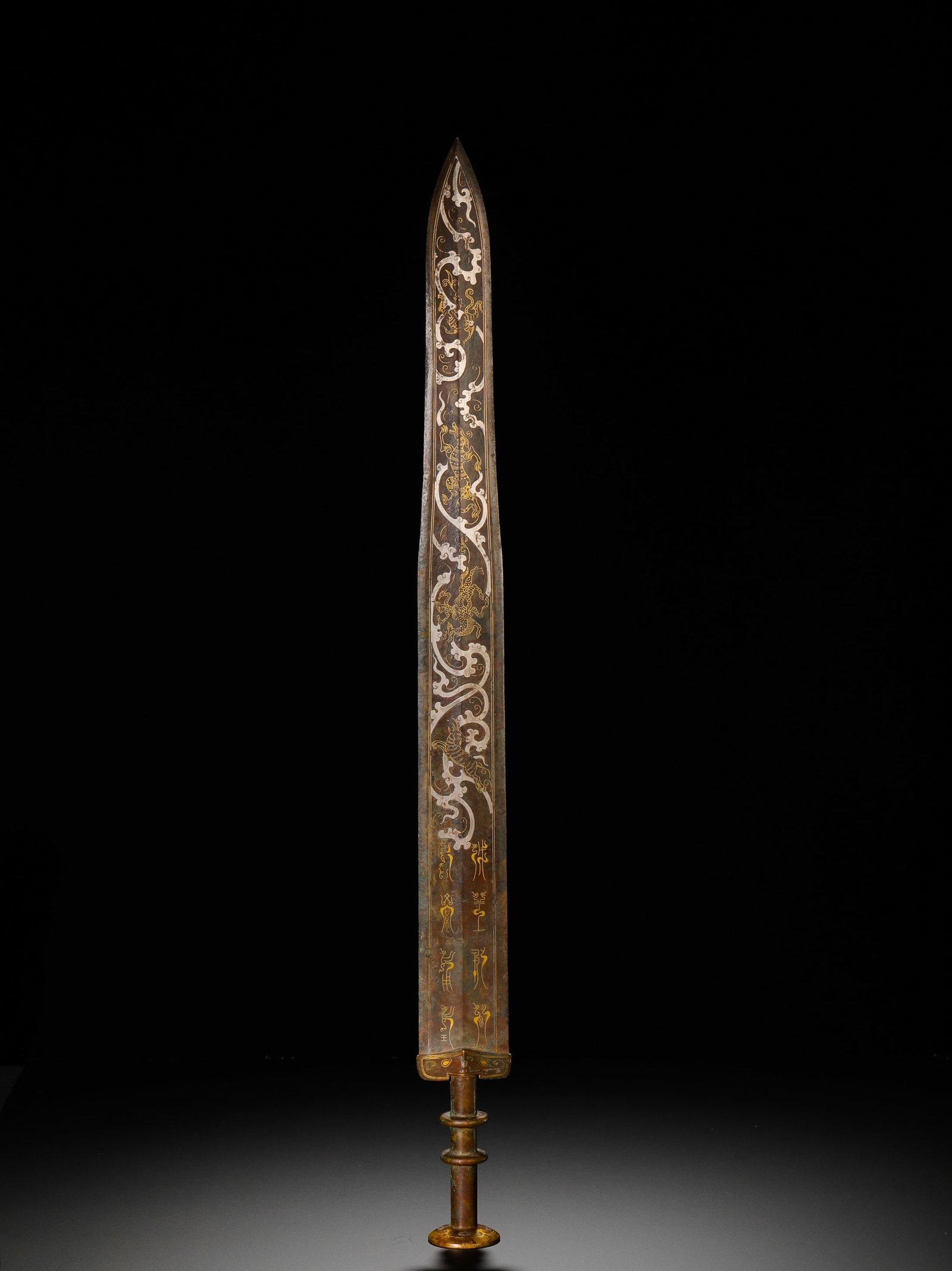 BRONZE SWORD WITH INLAID GOLD AND SILVER DRAGON PATTERNS FROM THE WARRING STATES PERIOD: Long:60.2cm(23.70in) Weight:900g(1.98lb)Warring States bronze long sword inlaid with gold and silver dragon patterns and inscriptions. The blade is decorated with silver-inlaid winding dragon and clou