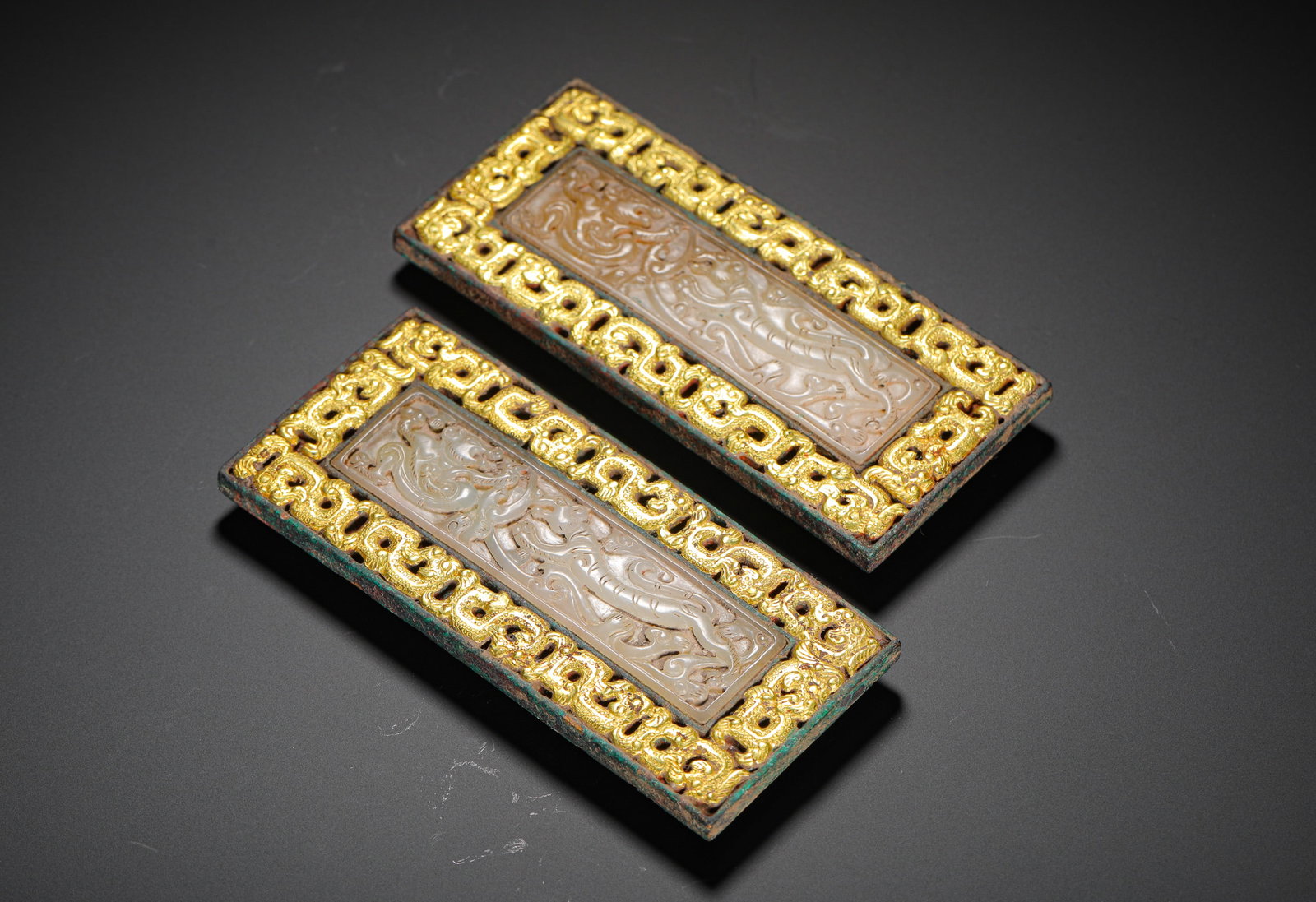BRONZE FROM THE WARRING STATES PERIOD WITH GILDED INLAID JADE BELT ORNAMENTS: H:11.5cm (4.53in) W:5cm (1.97in) Weight:560g (1.23lb)This pair of belt ornaments are Warring States Period garment fittings. Made of bronze with gilded edges, they feature a pierced jade carving of dr