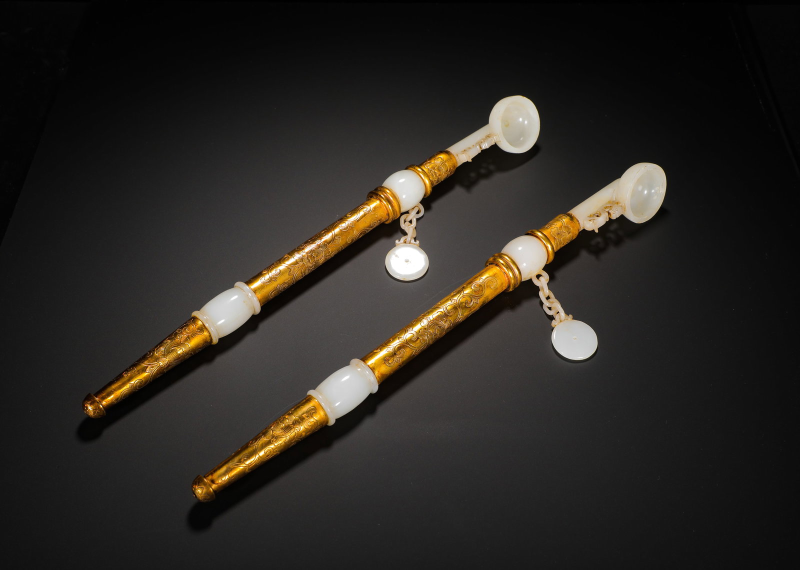 A PAIR OF GILDED FLOWER-ENCRUSTED HETIAN WHITE JADE CIGARETTE POLES FROM THE QING DYNASTY: L:40.5cmWeight:720gA pair of Qing Dynasty gilt bronze smoking pipes inlaid with Hetian white jade carved with interlocking floral scrolls, segmented with jade beads, each fitted with white jade bowl a