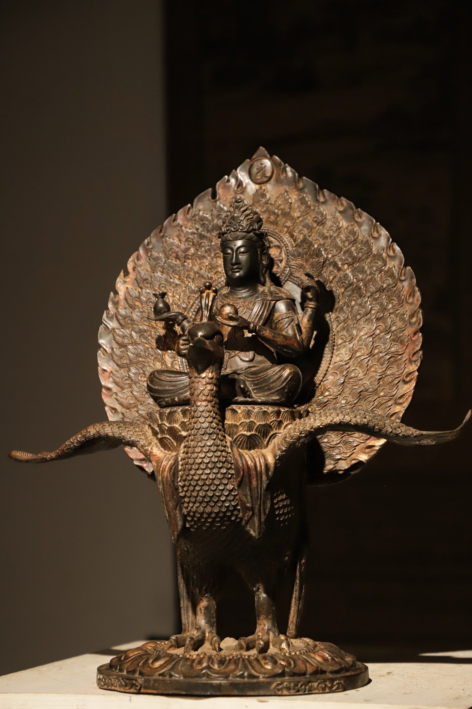 A BRONZE PEACOCK STATUE OF THE MING KING FROM THE YUAN DYNASTY: Height:45cm(17.72in) Width:40cm(15.75in) Weight:6000g(13.23lb)Antique bronze Mahamayuri peacock Buddha statue from Yuan-Ming period, carved feather mandorla, partial gilding, worshiped for warding off