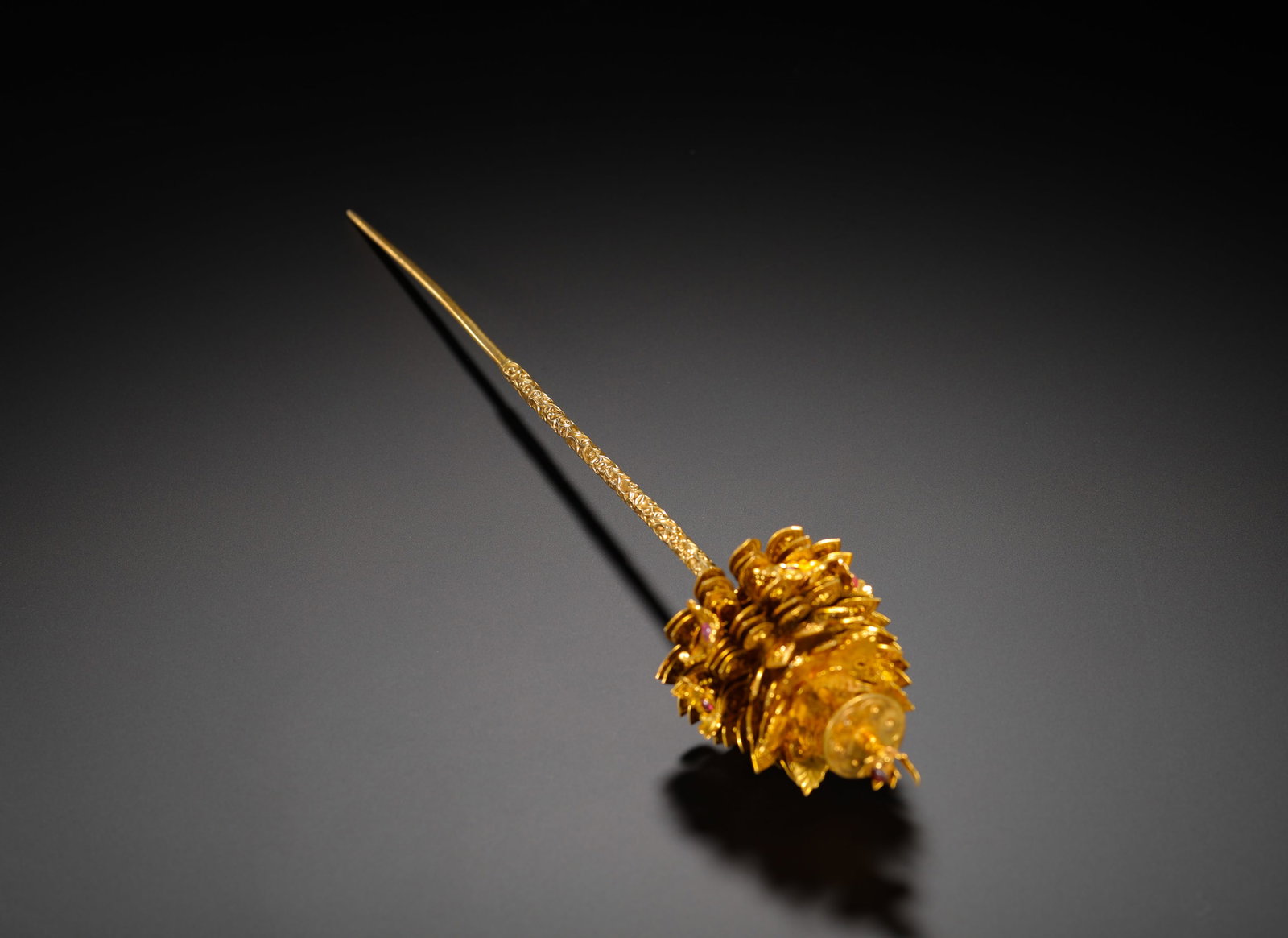 A GILDED BRONZE HAIRPIN INLAID WITH RUBIES: Long:35.5cm(13.98in) Width:6cm(2.36in) Weight:150g(0.33lb)Gilt bronze filigree hairpin inlaid with ruby, Qing Dynasty. The long pin shaft is fully chased with dense scrolling floral patterns. The head