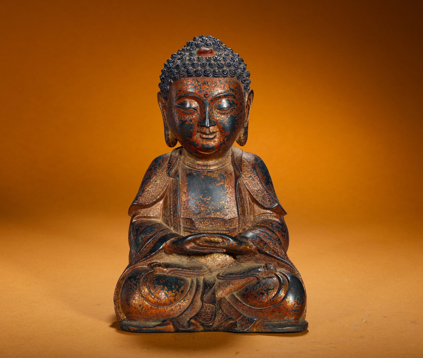 QING DYNASTY BRONZE LACQUERED GOLD STATUE OF SAKYAMUNI SITTING IN MEDITATION: Height:22cm(8.66in) Width:14cm(5.51in) Weight:1210g(2.67lb)Lacquered gilt bronze seated Shakyamuni Buddha in meditation mudra. Bronze body coated with black lacquer and worn gold-red patina. Tight spi