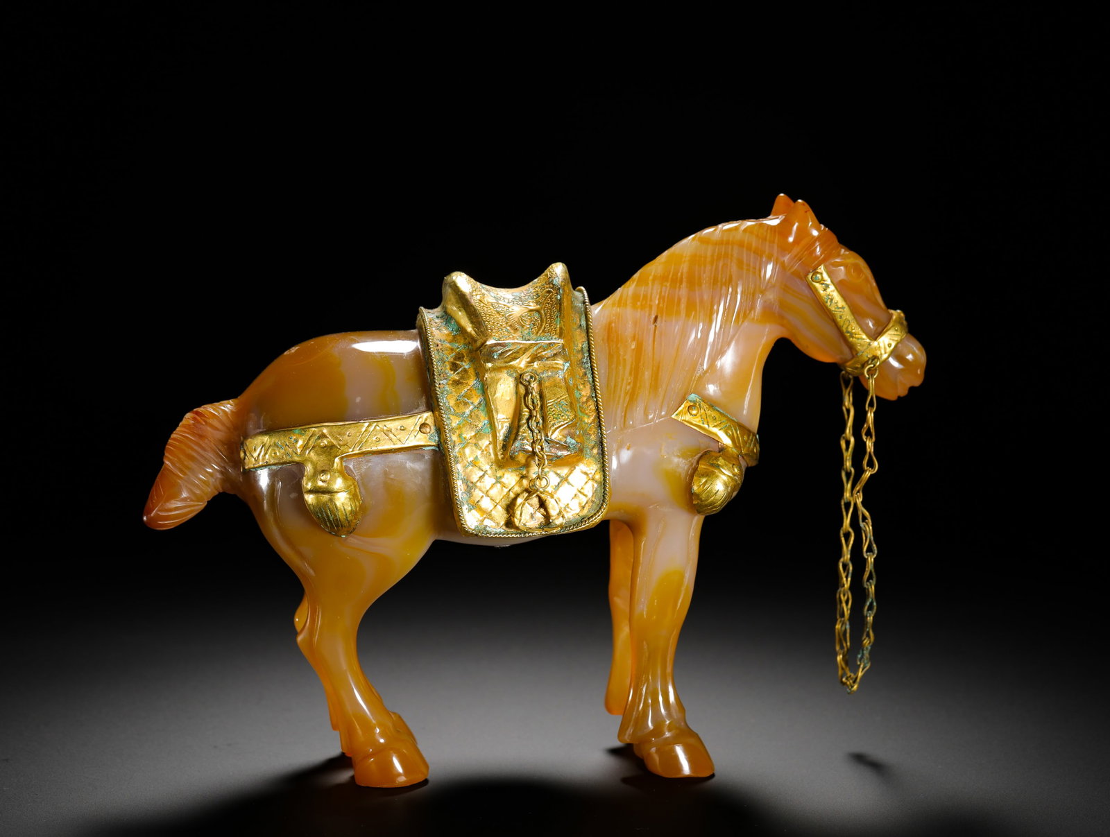 QING DYNASTY GOLD HORSE WRAPPED IN SILK AGATE: Height:14cm(5.51in) Width:20.5cm(8.07in) Weight:1020g(2.25lb)Qing Dynasty agate standing horse statue decorated with full gilt saddle and reins. Solid whole agate carving with natural orange-white ban