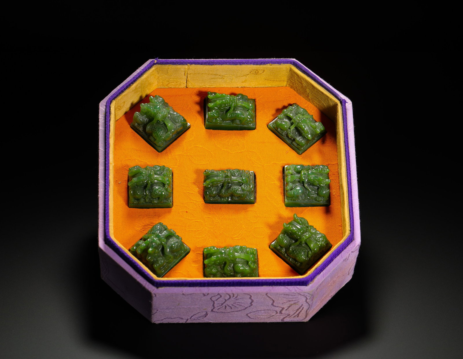 A SET OF HETIAN JADE NINE-DIRECTIONAL COILED DRAGON BUTTON JADE SEALS FROM THE QING DYNASTY: H:3cmW:4.1cmWeight:710gComplete set of nine Qing Dynasty Hetian spinach jade imperial seals with coiled dragon knobs, neatly carved square jade seals, housed in an original octagonal silk box lined wi