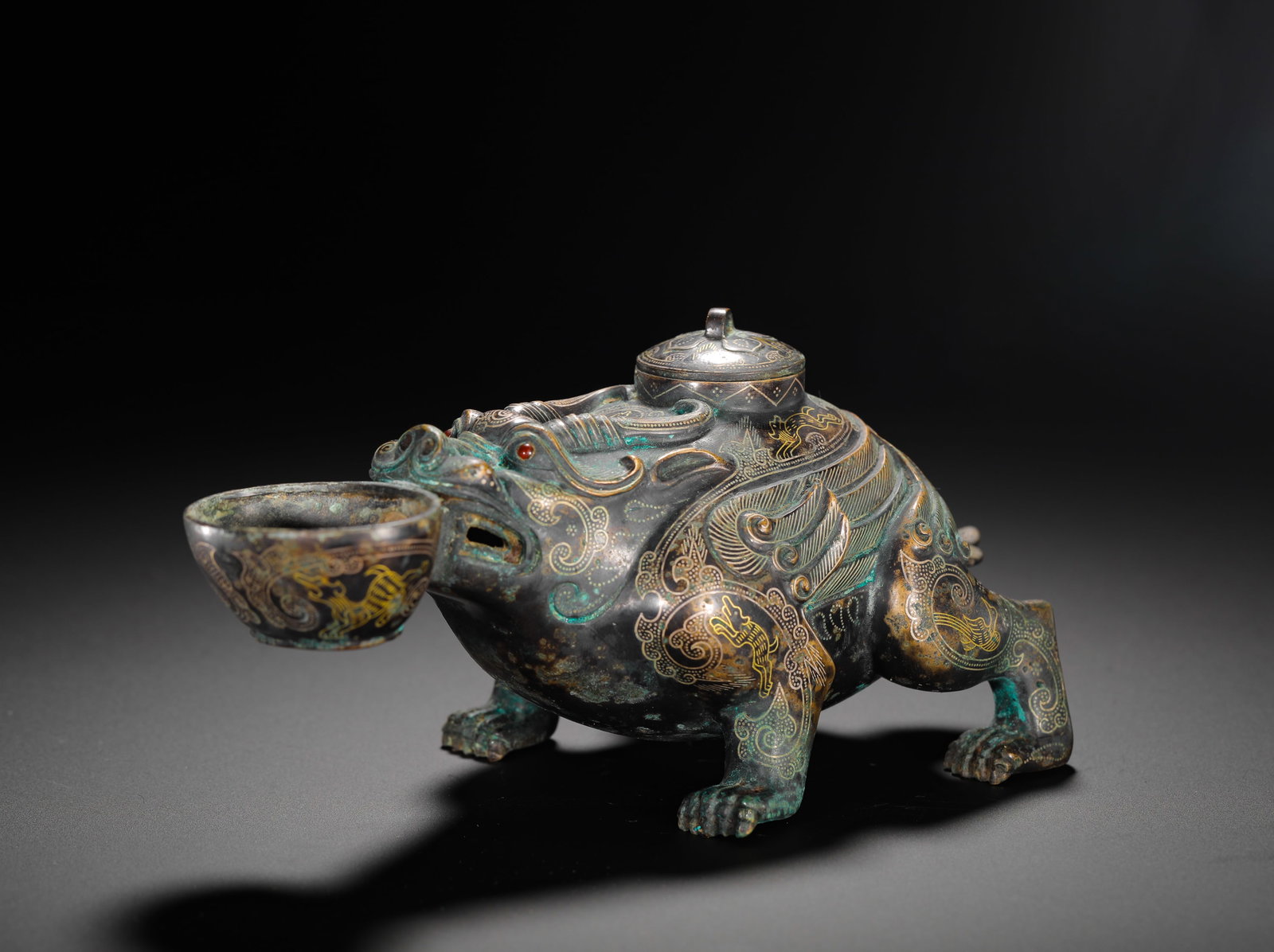 BRONZE WITH GOLD INLAID AUSPICIOUS BEAST HOLDING A CUP TO DRAW WINE FROM THE WARRING STATES PERIOD: Height:9cm(3.54in) Width:17cm(6.69in) Weight:600g(1.32lb)Warring States bronze wine vessel with gilded mythical beast holding a cup, interwoven animal engravings and golden inscribed text on base, a