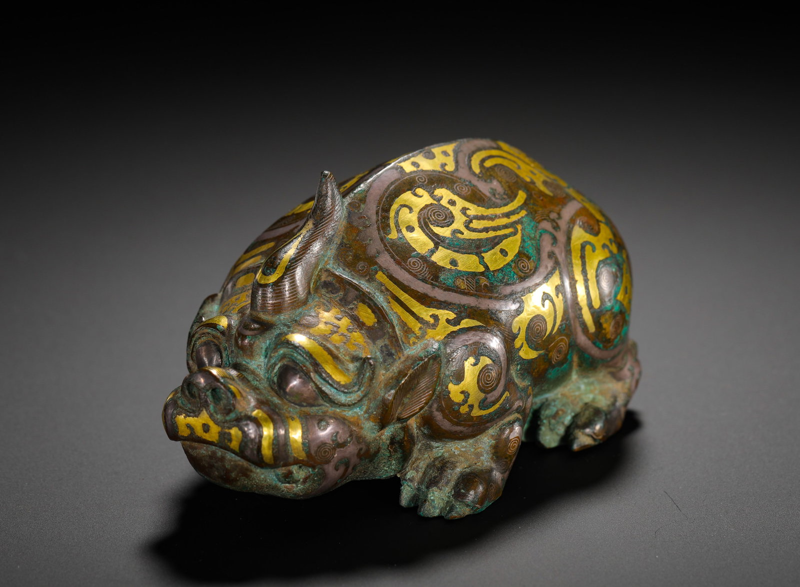 BRONZE INLAID WITH GOLD AND SILVER FROM THE WARRING STATES PERIOD, A ONE-HORNED AUSPICIOUS BEAST: Height:8cm(3.15in) Width:12cm(4.72in) Weight:560g(1.23lb)Warring States bronze paperweight shaped like a single-horned mythical beast, decorated with gilded scroll cloud patterns, an ancient desk orna