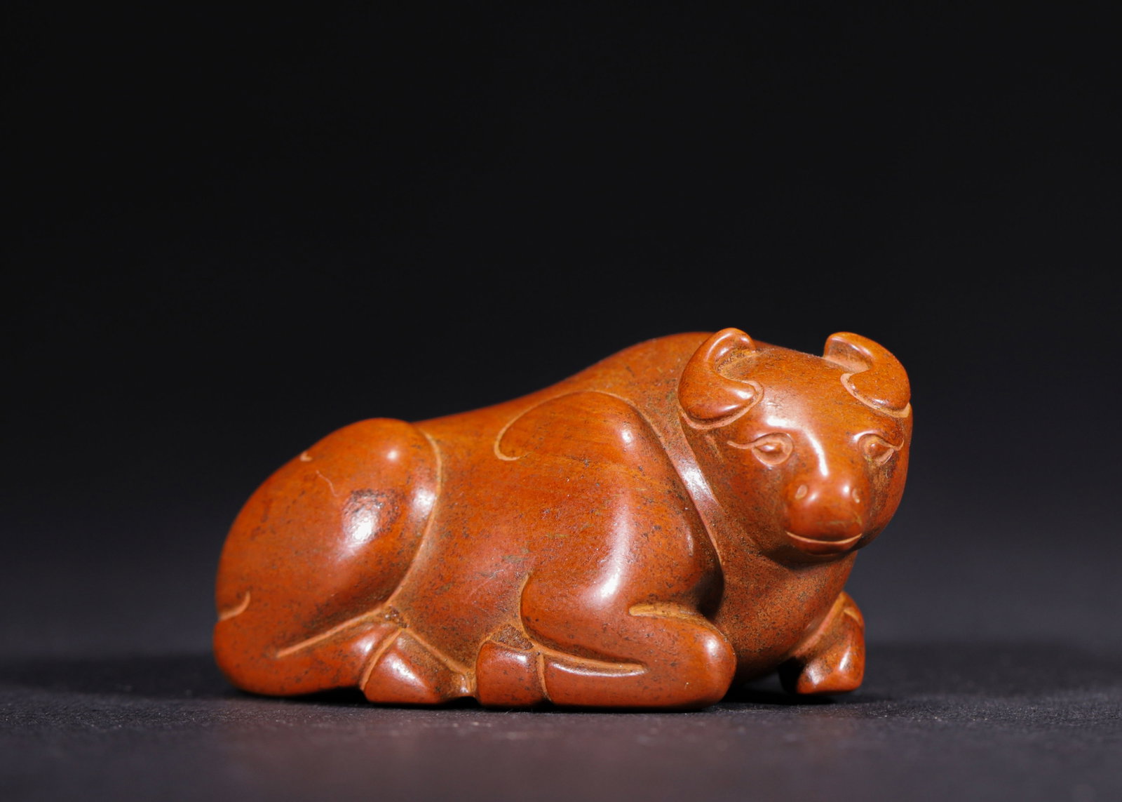 CRIMSON PATINATED AGATE RECUMBENT OX, HAN DYNASTY (202 BC-220 AD): H 2.8cm (1.10 in); L 5.5cm (2.17 in); W 3cm (1.18 in); Wt 64g (0.14 lb),Agate thoroughly permeated by rich crimson patina. Fully carved recumbent ox with plump body rendered in fluid, succinct lines, 