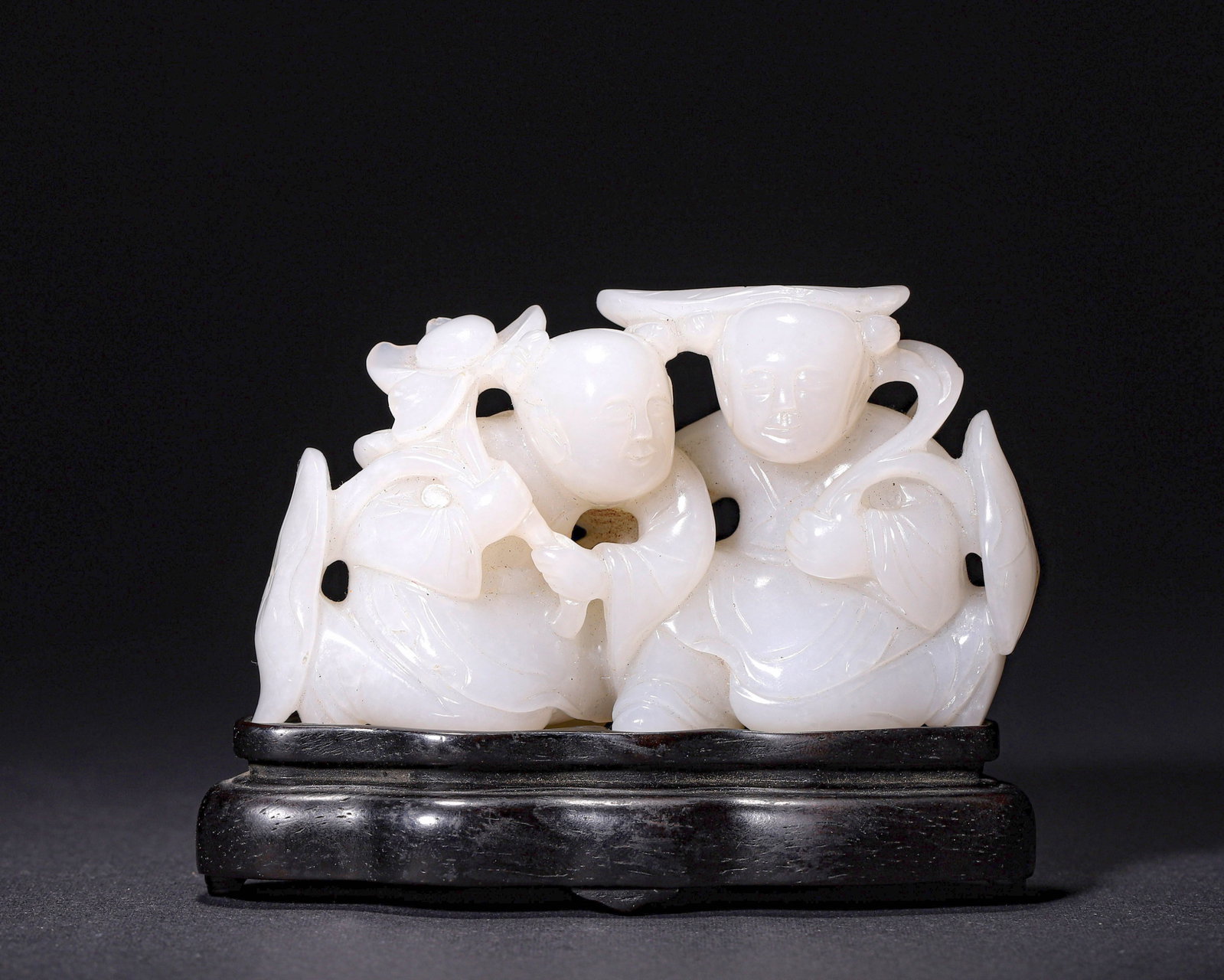 A WHITE HETIAN JADE HE-HE ER XIAN GROUP, QING DYNASTY (1636?C1912): L 9.00cm (3.54 in); W 3.00cm (1.18 in); H 5.50cm (2.17 in); Wt 180.00g (0.40 lb),Carved from white Hetian jade of creamy luster with minor russet inclusions. Two immortals seated in embrace, one holdi
