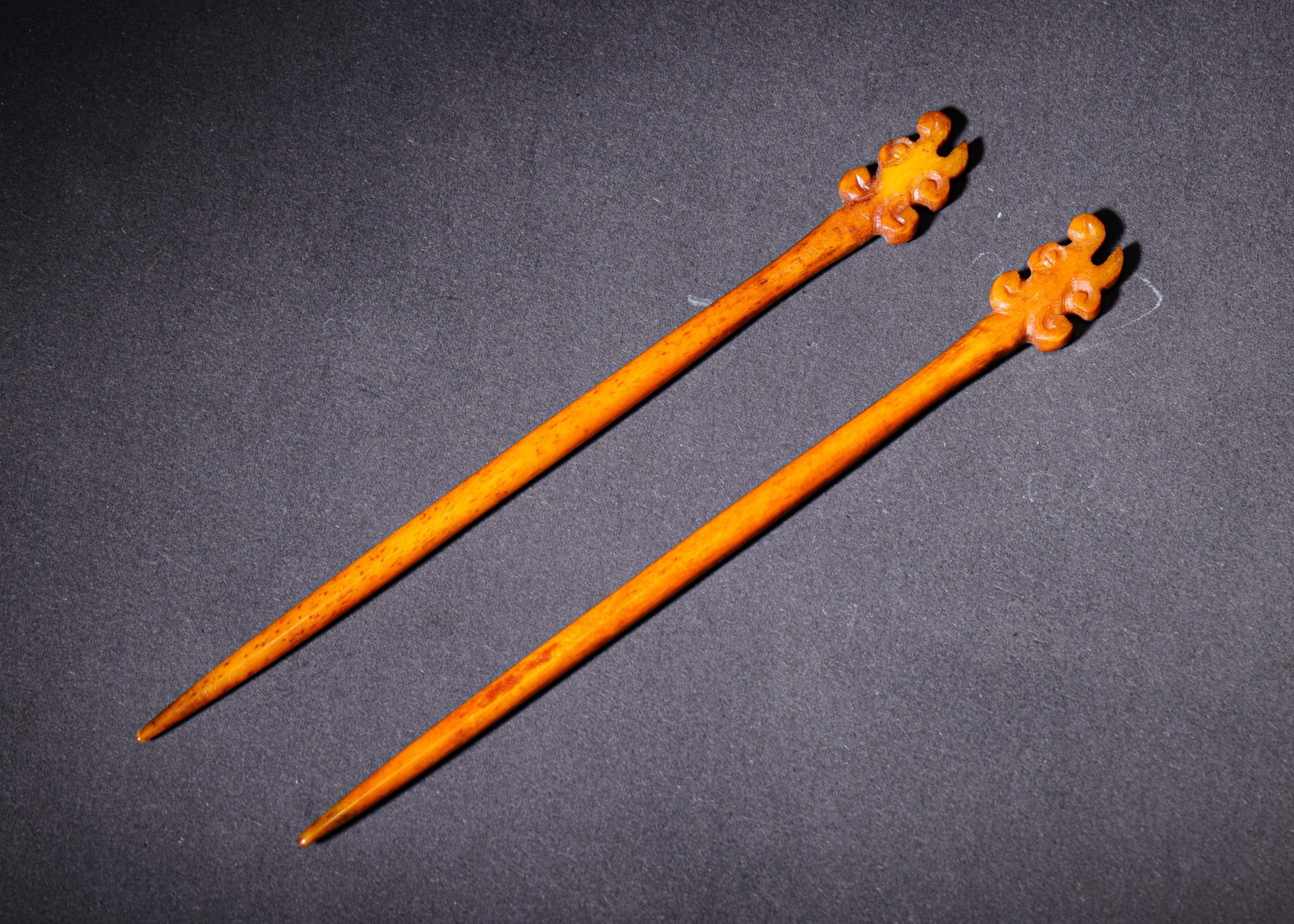 A PAIR OF CARVED BONE HAIRPINS WITH RUYI HEADS (QING DYNASTY, 1636-1912 AD): L 15cm (5.91 in),Carved from animal bone with warm honey-toned patina. The terminals are decorated with stylised ruyi scrolls. Slender plain shafts taper to fine points. A matched pair of traditional 