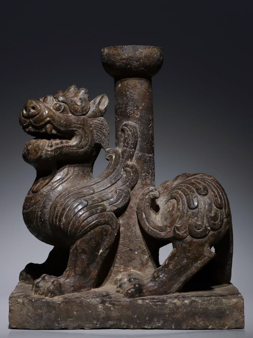 BLUESTONE CANDLESTICK WITH TIANLU MYTHICAL BEAST, HAN DYNASTY (202 BC?C220 AD): H 41cm (16.14 in); L 34cm (13.39 in); W 23cm (9.055 in),Carved from a single bluestone block, modelled as a recumbent winged Tianlu beast upon rectangular plinth, with layered feather patterns incised