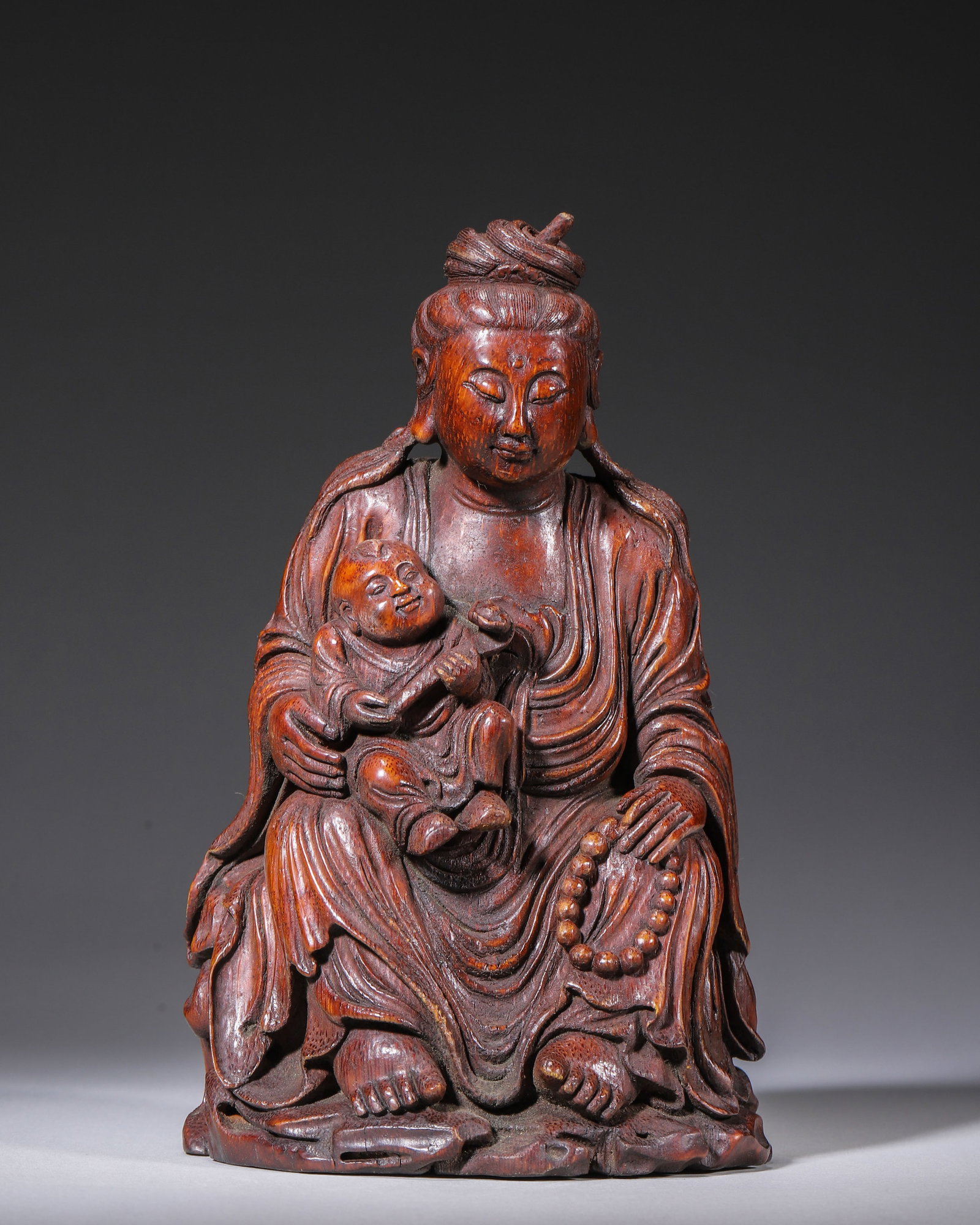QING BAMBOO CARVED CHILD-GIVING GUANYIN, SIGNED TIANZHANG: L 12.00cm (4.72 in); W 11.00cm (4.33 in); H 20.00cm (7.87 in); Wt 723.00g (1.59 lb),Carved from a single aged bamboo root, with warm reddish-brown patina built up over long handling and distinct