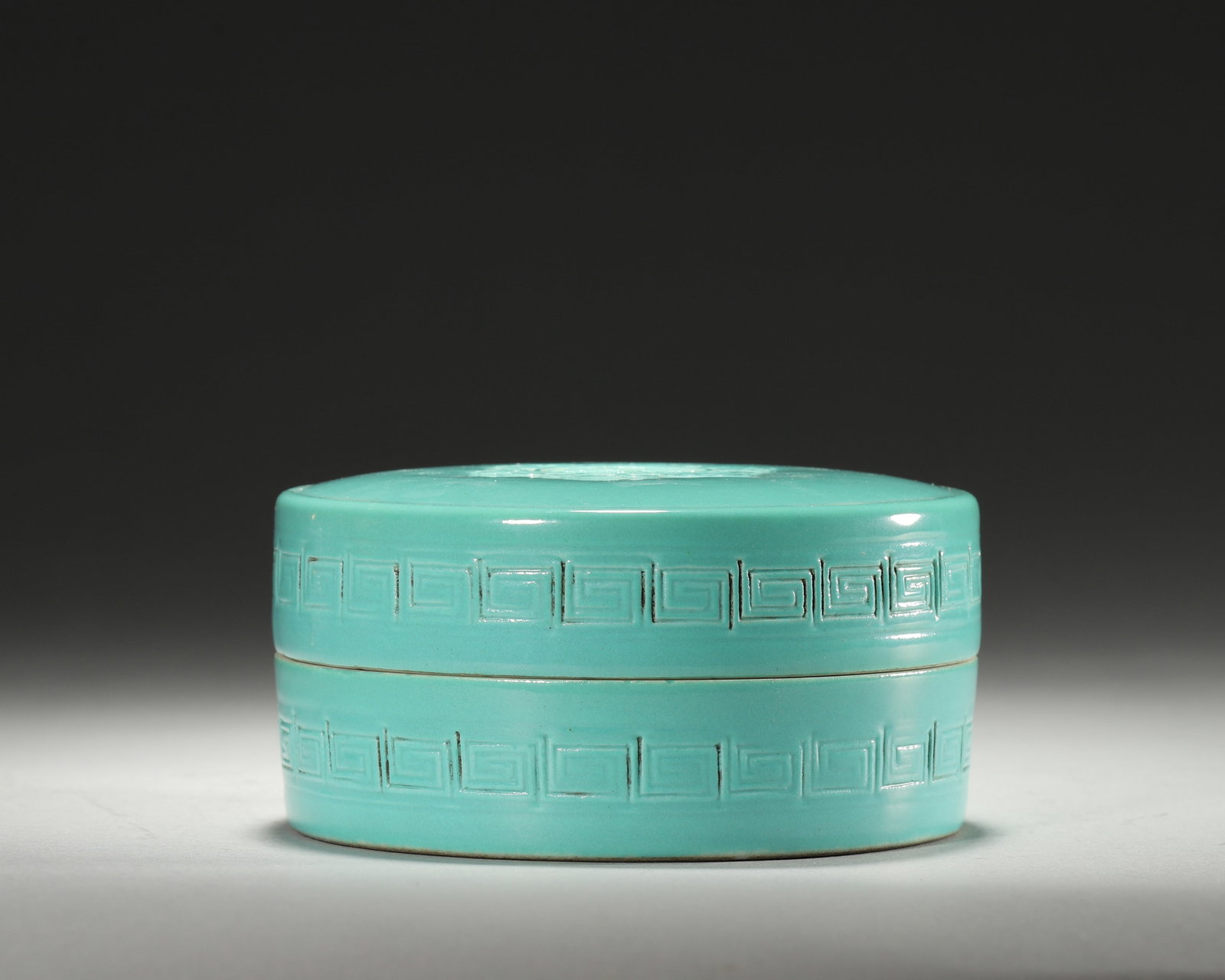 TURQUOISE-GLAZED COVERED BOX WITH RELIEF SHOU AND CLOUD MOTIFS, QIANLONG PERIOD, QING DYNASTY: D 9.5cm (3.74 in); H 4.7cm (1.85 in); Wt 393g (0.87 lb),Flattened circular box with fitted cover, fully covered in even turquoise glaze. The lid moulded with central shou character encircled by cloud 