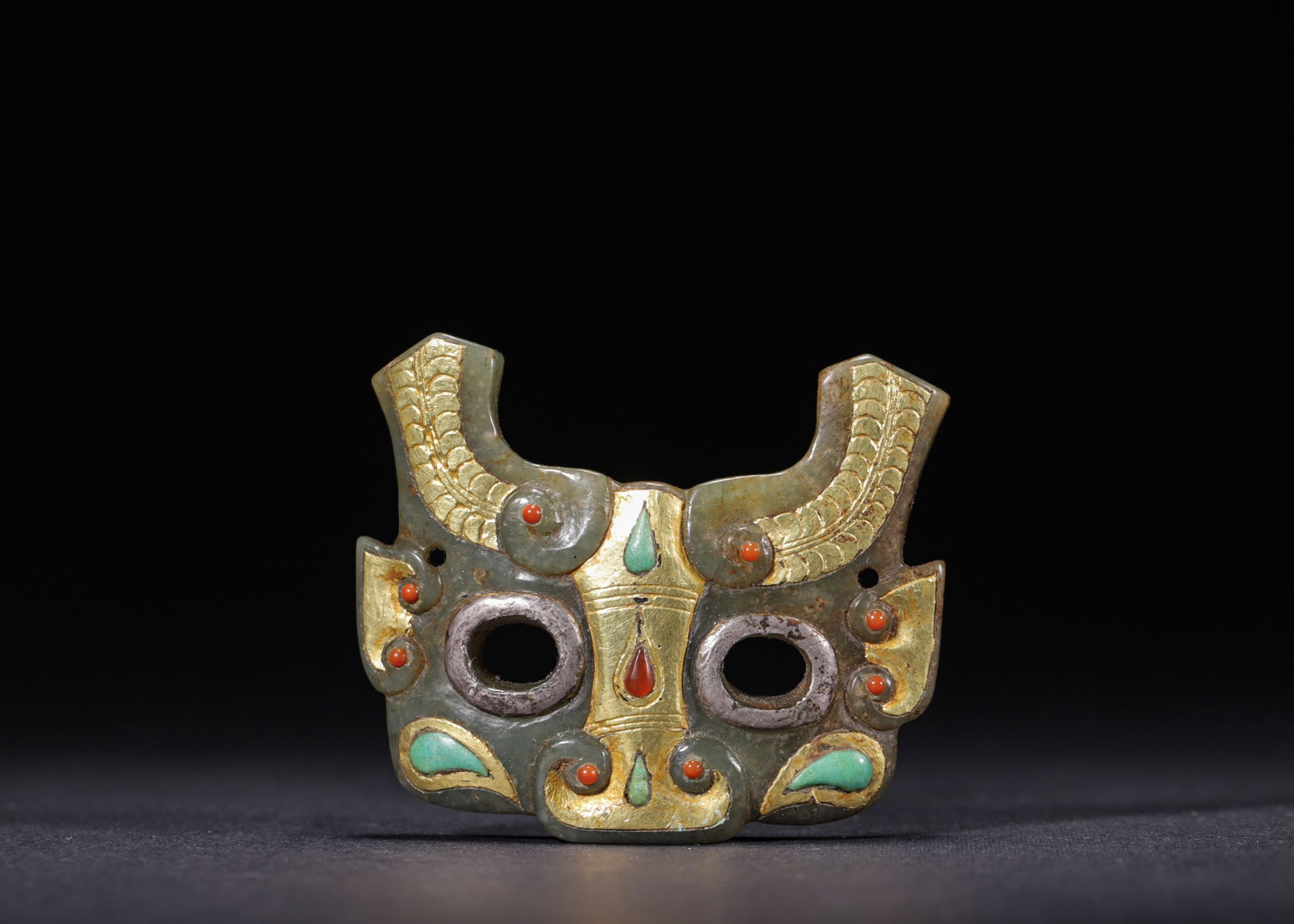 HETIAN JADE BEAST-FACE ORNAMENT DECORATED WITH GOLD & SILVER PAINTING, INLAID CARNELIAN AND: L 6cm (2.36 in); H 5cm (1.97 in); Wt 14g (0.031 lb),Carved from Hetian green jade in beast-face shape. Gold and silver painting adorns the horns and nasal patterns, while carnelian and turquoise are i