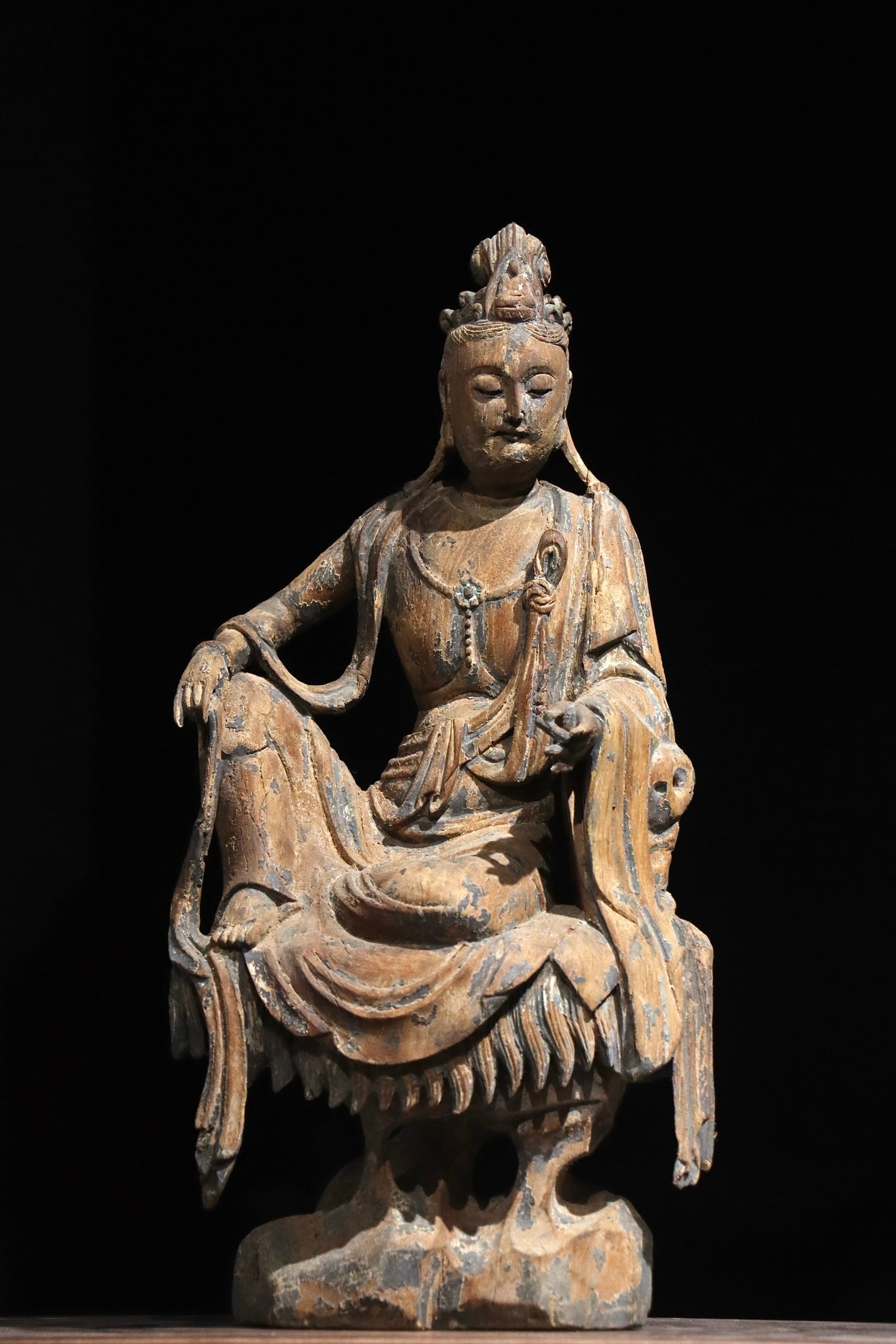 SONG DYNASTY, WOOD CARVED SEATED AVALOKITESHVARA IN RELAXED POSE (960?C1279): H 47cm (18.504 in),Wood-carved Avalokiteshvara in lalitasana. The deity bears a serene countenance with neat headdress, draped celestial robes and neck ornaments. Fluid folds define the garment. Trace
