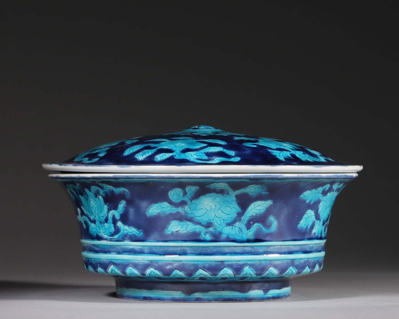 A COVERED BASIN WITH FOUR SEASONS FLOWERS IN TURQUOISE ENAMEL ON BLUE GROUND, XUANDE PERIOD, MING: L 19cm (7.48 in); H 9cm (3.54 in),Ming Xuande covered flared-rim basin with domed lid and knob. Deep cobalt blue ground overlaid with raised turquoise enamel floral reliefs. Lid centred on a treasure 