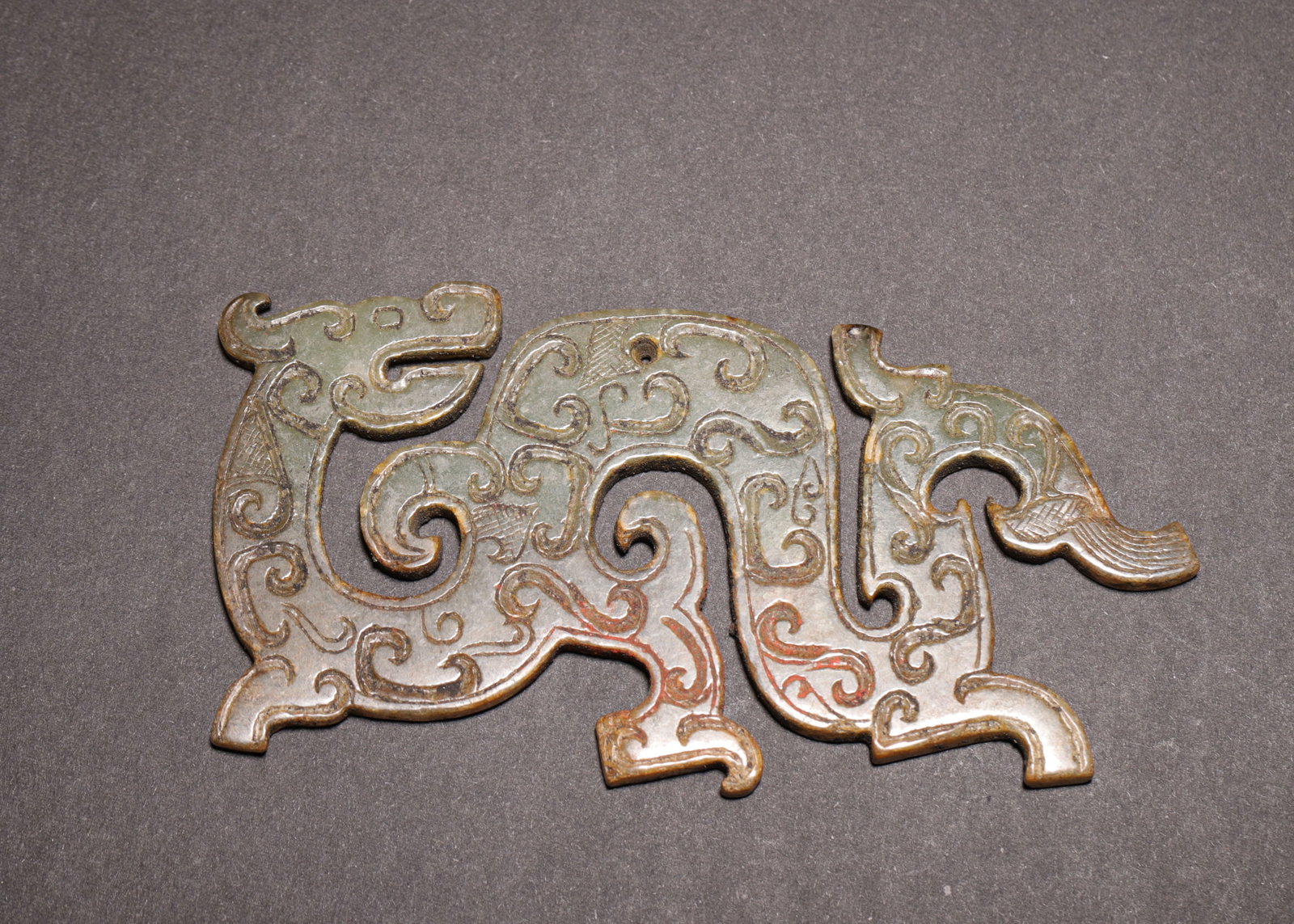 ARCHAIC JADE RECUMBENT DRAGON PENDANT, WARRING STATES PERIOD (475?C221 BC): L 11cm (4.33 in); W 5.5cm (2.17 in); Wt 59g (0.13 lb),Carved from greenish-white jade with burial patina. Openwork pendant modelled as a striding dragon turning its head backward. The surface incised 