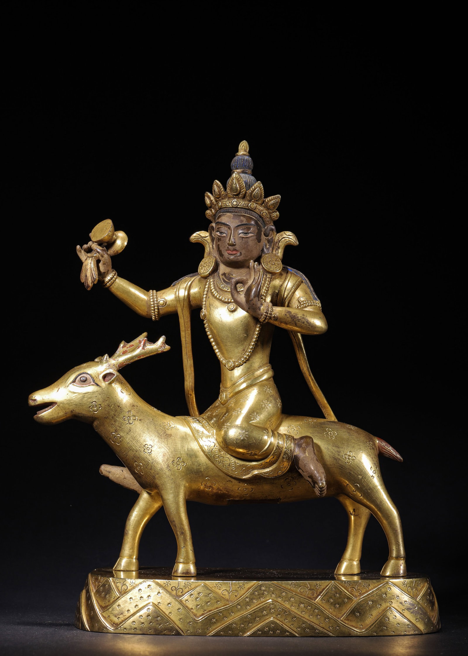 GILT COPPER DHARMA PROTECTOR SEATED ON DEER, QING DYNASTY (1644-1912 AD): L 21cm (8.27 in); W 12cm (4.72 in); H 28cm (11.024 in); Wt 3489g (7.69 lb),Cast copper fully covered with gilding. The crowned deity with polychrome facial details rides astride a sacred deer. Right h