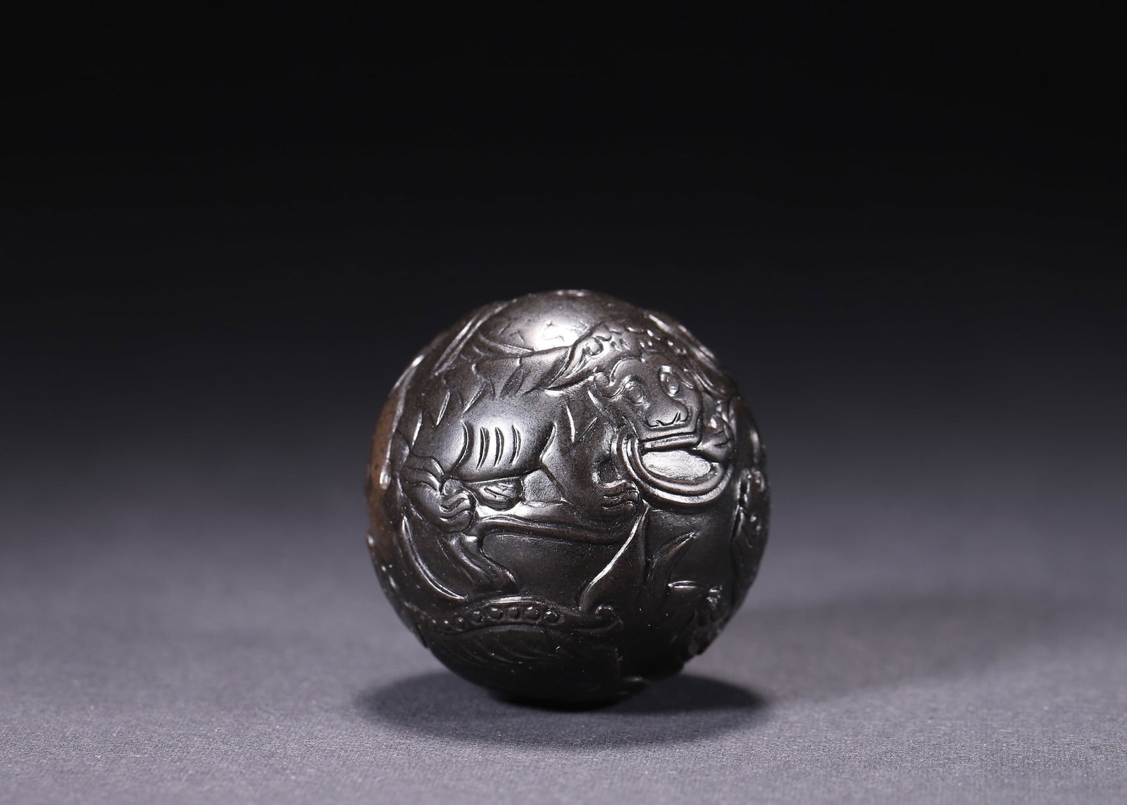 HAN DYNASTY (206 BC-220 AD) FULLY CALCIFIED JADE BEAD CARVED WITH AUSPICIOUS BEASTS: Wt 84g (0.19 lb); D 3.8cm (1.496 in),Jade bead fully permeated with black patina. High relief carving of multiple auspicious beasts across the surface. The beasts are rendered in dynamic poses with po