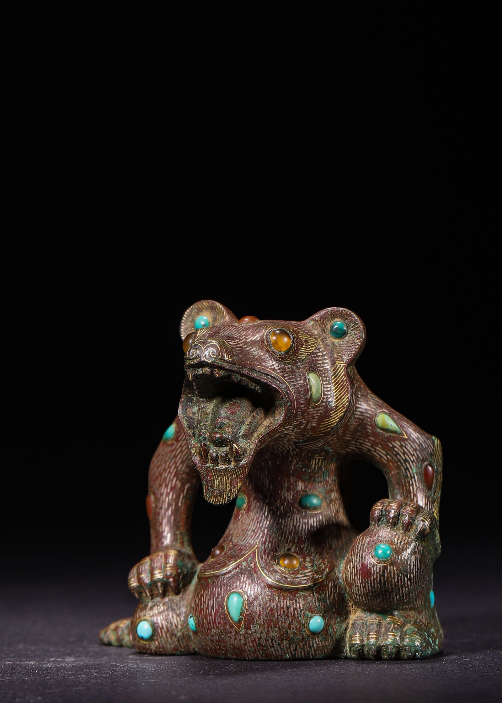 BRONZE BEAR WEIGHT INLAID WITH GOLD, SILVER, TURQUOISE AND AGATE, HAN DYNASTY (202 BC?C220 AD): L 7cm (2.76 in); W 5.5cm (2.17 in); H 6cm (2.36 in); Wt 296g (0.65 lb),Bronze mat weight modelled as a squatting bear. The bear raises its head with open jaws, presenting a powerful posture. Fine fur 