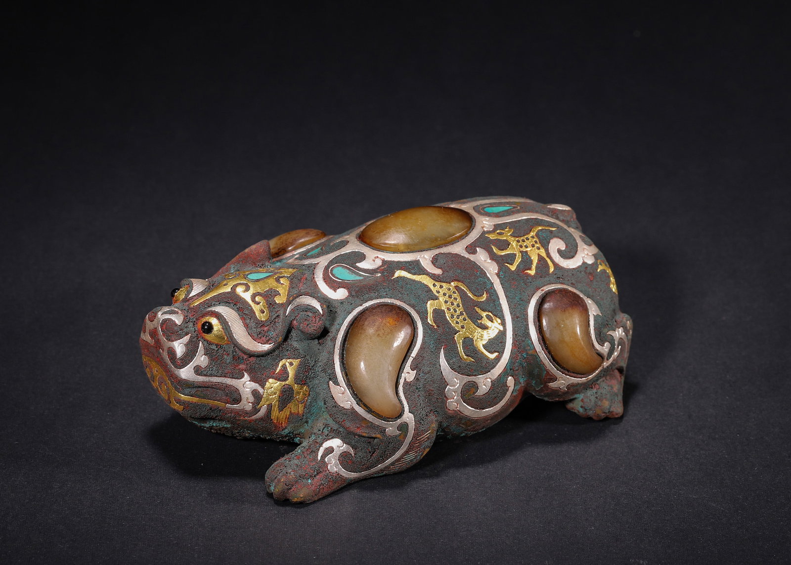 BRONZE MYTHICAL BEAST WEIGHT INLAID WITH GOLD, SILVER AND JADE, HAN DYNASTY (202 BC?C220 AD): H 5.5cm (2.17 in); L 12cm (4.72 in); W 7.5cm (2.95 in); Wt 534g (1.18 lb),Cast bronze weight modelled as a recumbent mythical beast. The surface decorated with inlaid gold and silver scroll outlines, 