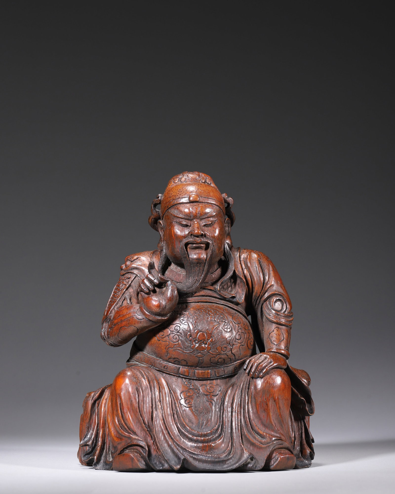 QING DYNASTY BAMBOO CARVED SEATED STATUE OF GUAN GONG, SIGNED YUNSHENG: L 14.00cm (5.51 in); W 12.00cm (4.72 in); H 18.00cm (7.09 in); Wt 543.00g (1.20 lb),Carved from a single aged bamboo root with distinct grain and glossy reddish patina. Guan Gong seated at ease, weari