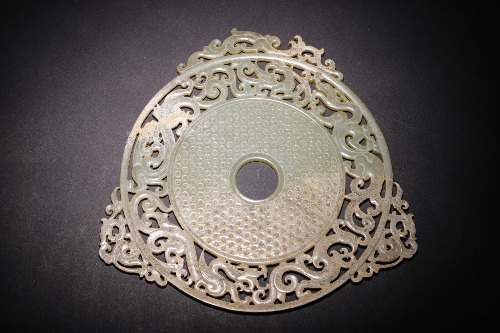 CELADON WHITE JADE OPENWORK BI WITH DRAGON, PHOENIX AND GRANULE PATTERN, HAN DYNASTY (202 BC-220 AD): L 21cm (8.27 in); W 21cm (8.27 in); Wt 358g (0.79 lb),Carved from Hetian celadon white jade with natural ancient patina. The disc is densely covered with orderly granule patterns. The outer rim featur