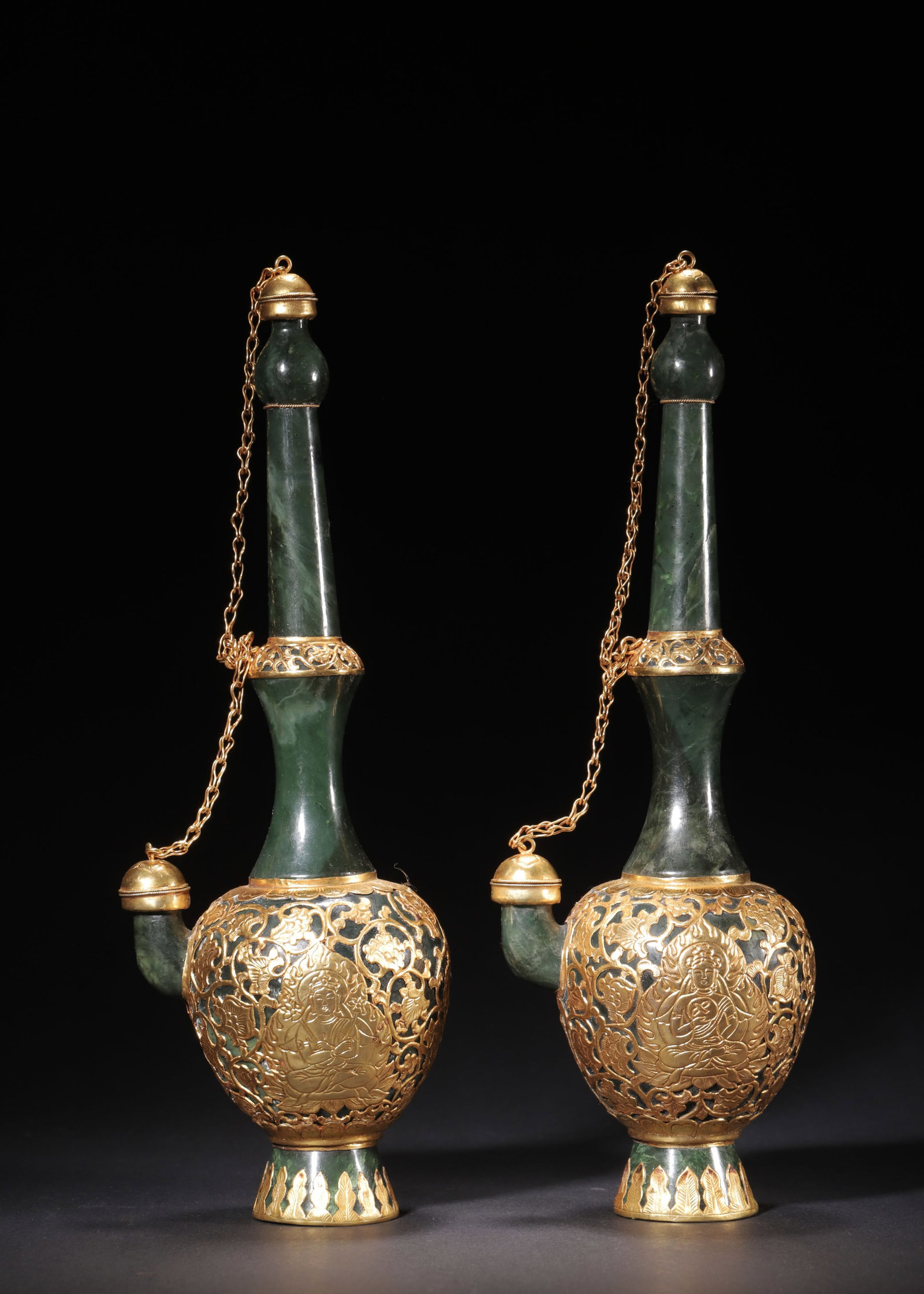 A PAIR OF SPINACH JADE EWERS WITH OPENWORK GILT MOUNTS, QING DYNASTY (1644-1912 AD): H 30cm (11.81 in); L 10cm (3.94 in); W 8cm (3.15 in); Wt 1451g (3.20 lb),Carved from single spinach jade boulders. Tall slender neck, globular body with spout linked to cap by gilt chain. The body ove