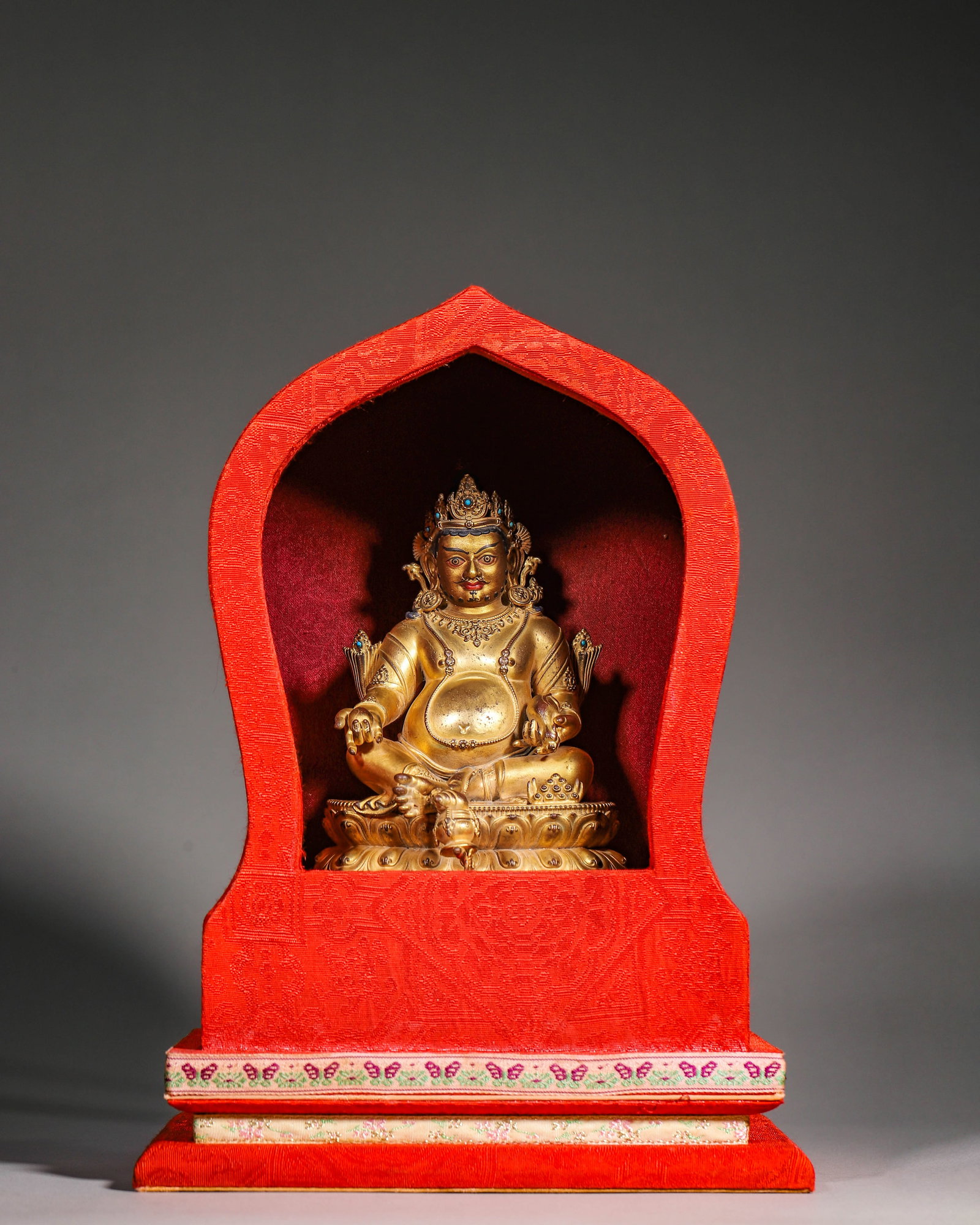 QING DYNASTY GILT BRONZE STATUE OF JAMBHALA, WITH ORIGINAL SILK SHRINE: Figure L 12cm (4.72 in); Figure W 11cm (4.33 in); Figure H 16cm (6.299 in); Wt 1027g (2.26 lb),Gilt bronze seated Jambhala of Qing dynasty. Turquoise-inlaid crown, rounded face with pigment details. R