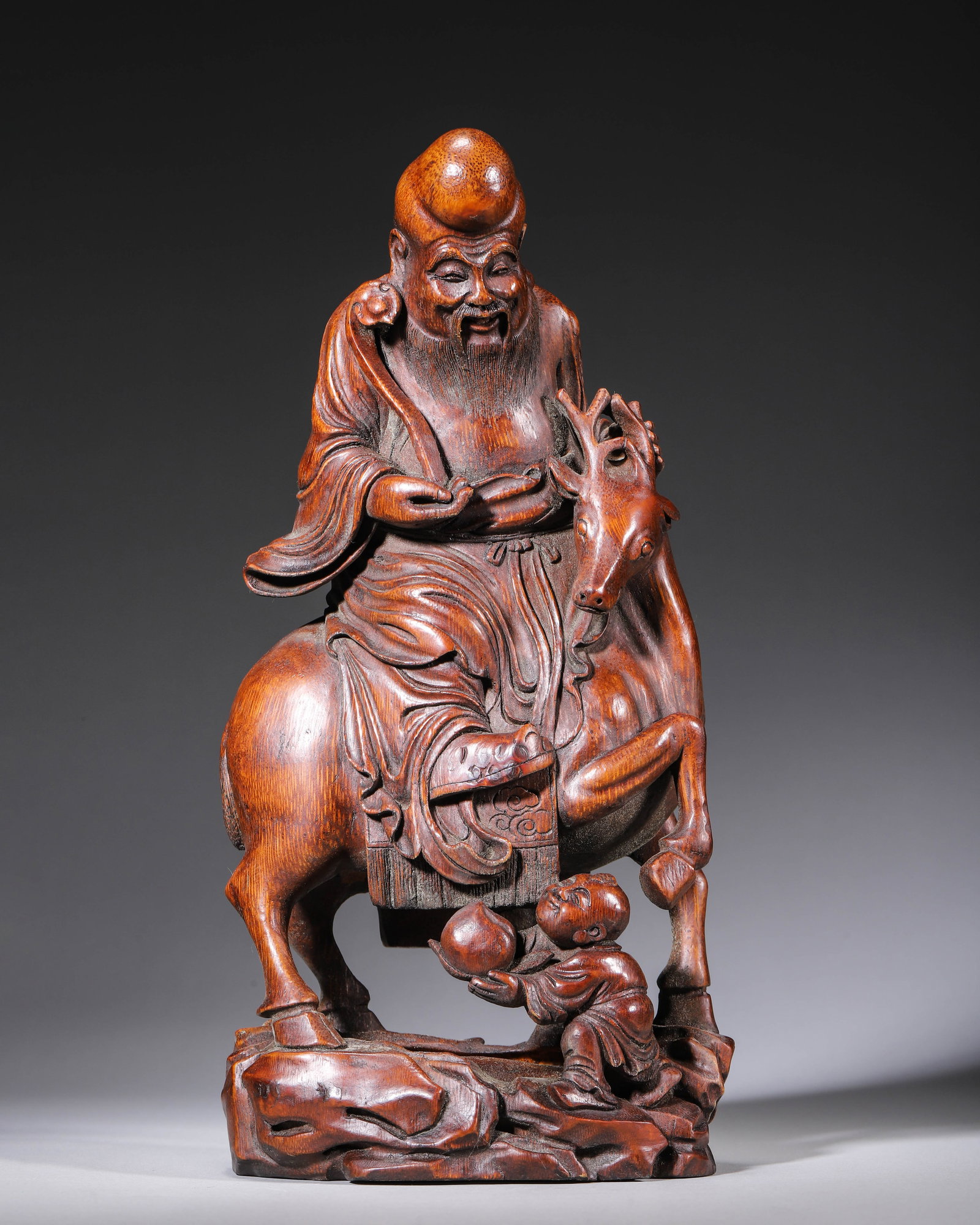QING DYNASTY BAMBOO ROOT CARVED GOD OF LONGEVITY ON DEER WITH PEACH-OFFERING BOY, SIGNED TIANZHANG: L 13.00cm (5.12 in); W 9.00cm (3.54 in); H 27.00cm (10.63 in); Wt 623.00g (1.37 lb),Entirely carved from aged bamboo root with warm reddish-brown antique patina. The God of Longevity rides a sacred de